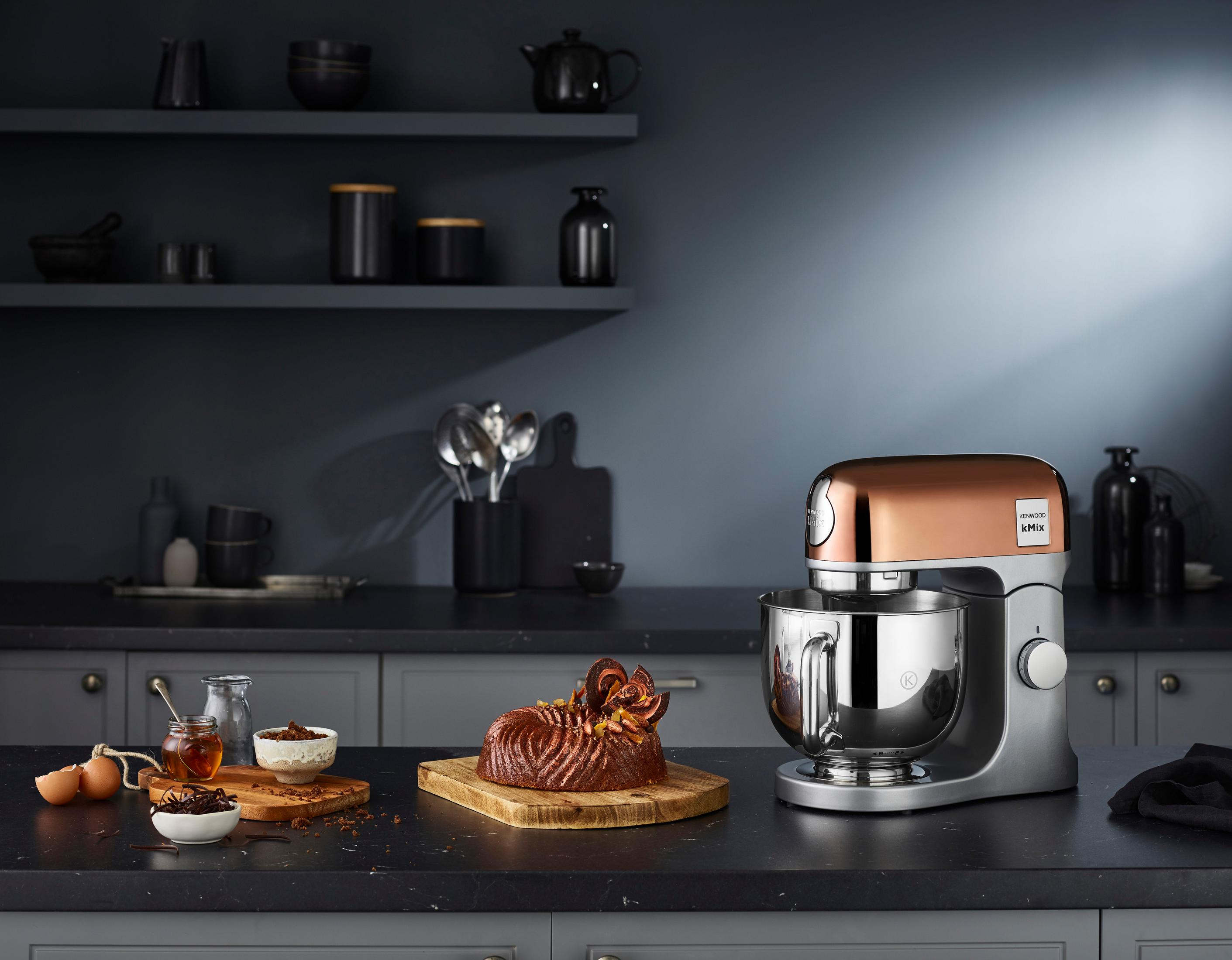 Cucina con miscelatore in rame, torta e ingredienti su un piano scuro.