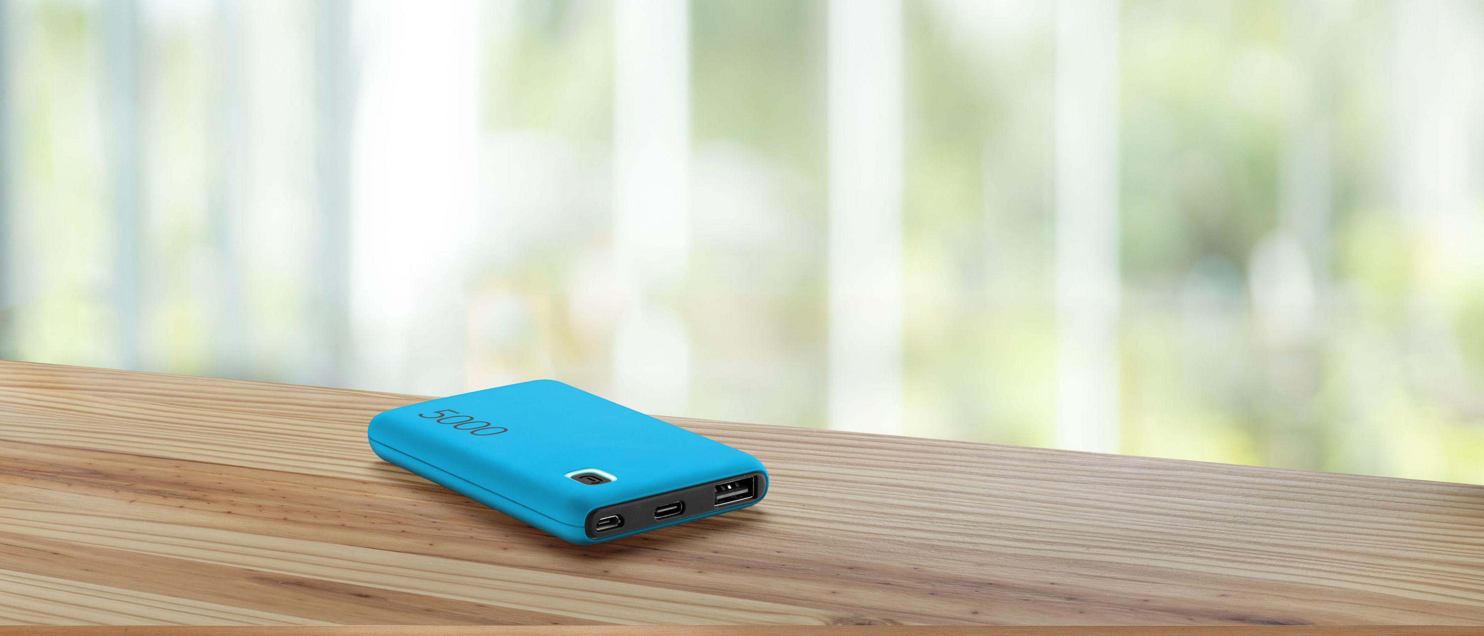 Un power bank blu su un tavolo di legno. Lo sfondo mostra una finestra sfocata.