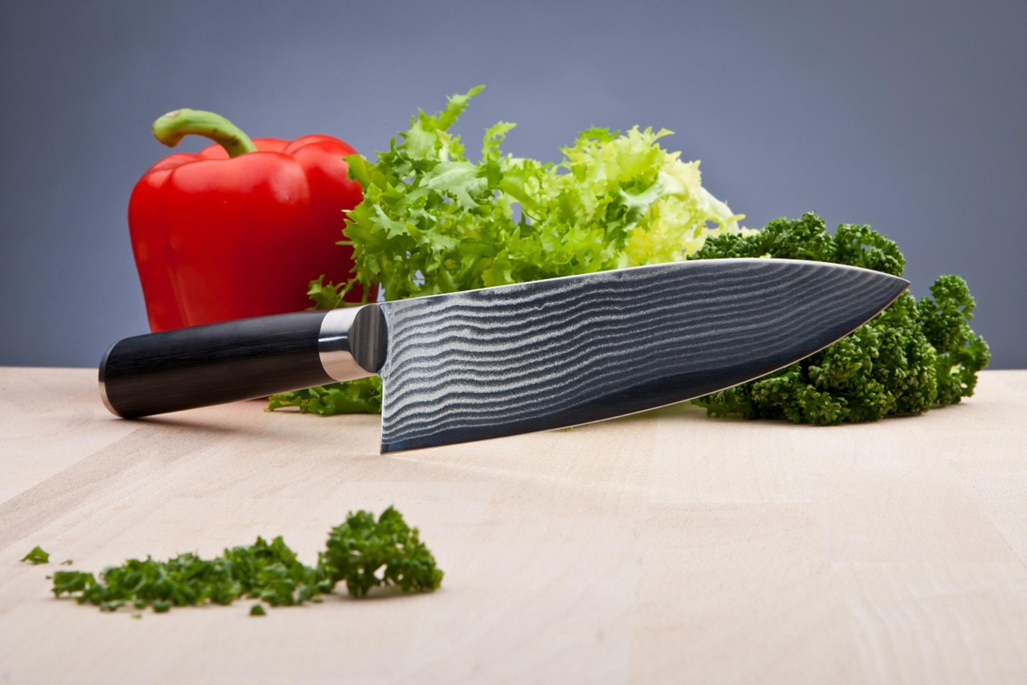 Küchenmesser mit schwarzem Griff, roter Paprika, Salat und Petersilie auf einem Holzbrett.