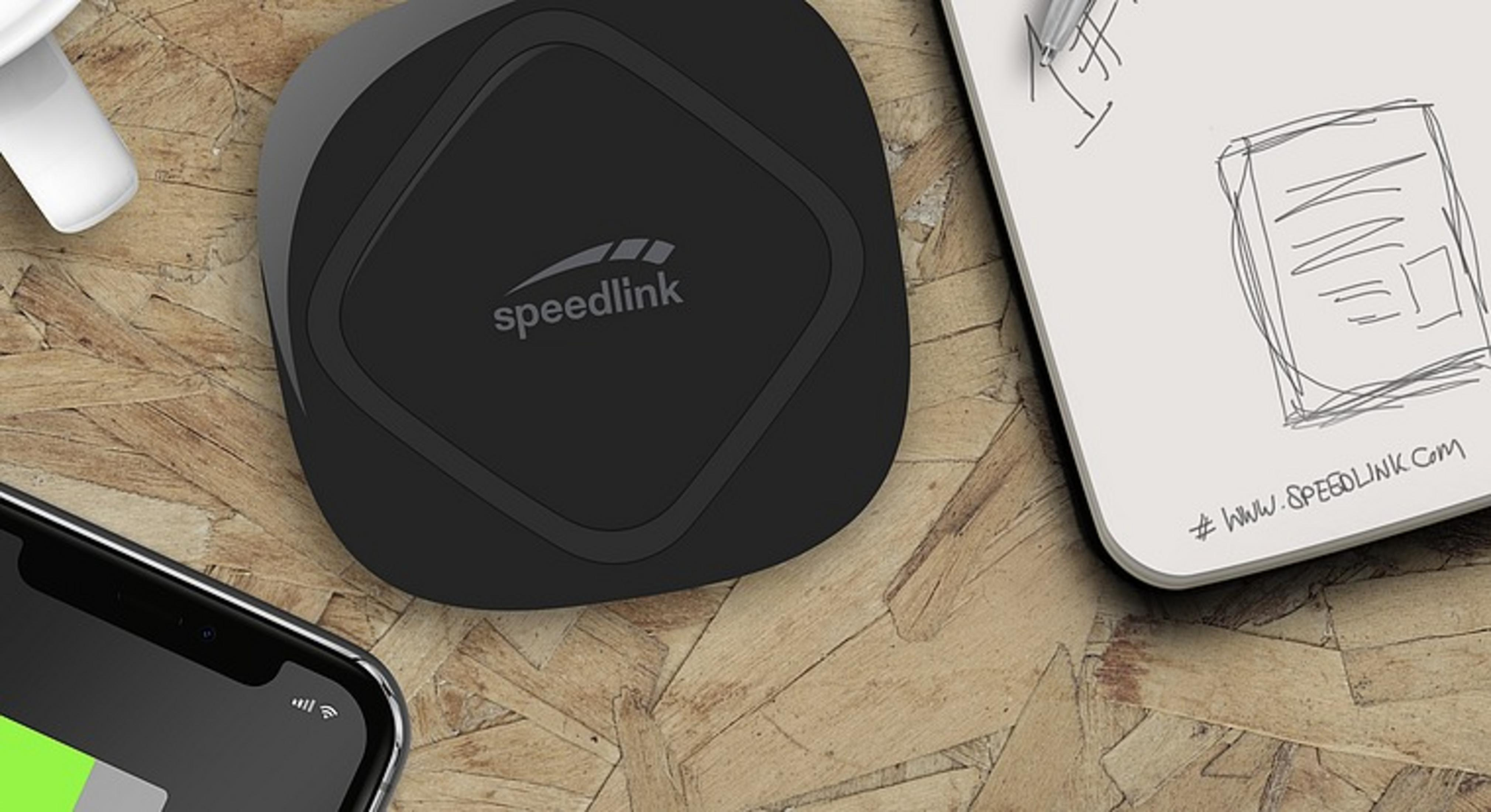 Schwarzes Speedlink-Gerät auf einem Holztisch, mit Notizblock und Telefon. Das Telefon hat einen grünen Balken.