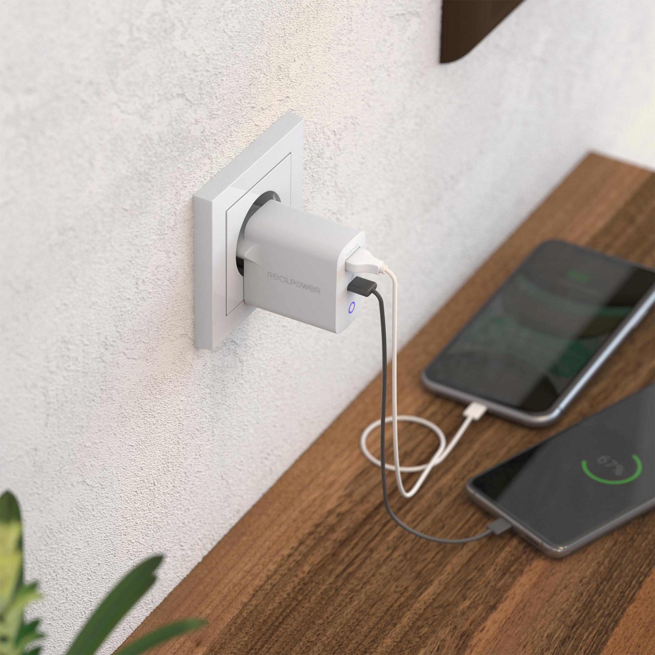 White REOLPOWER charger plugged into a wall outlet, charging two phones on a wooden table.