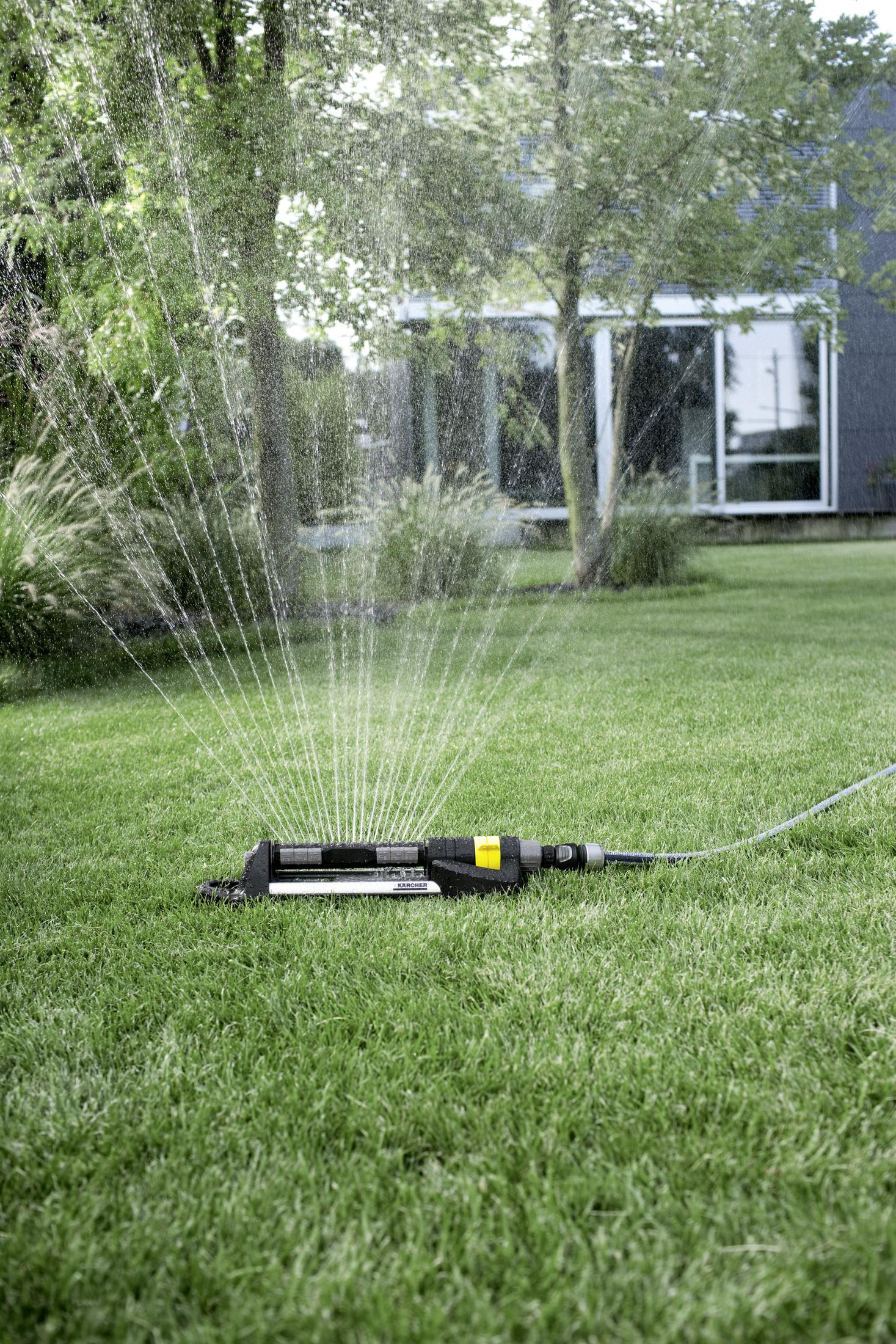 Ein Rasensprenger, der Wasser nach oben sprüht, mit grünem Gras und Bäumen im Hintergrund.