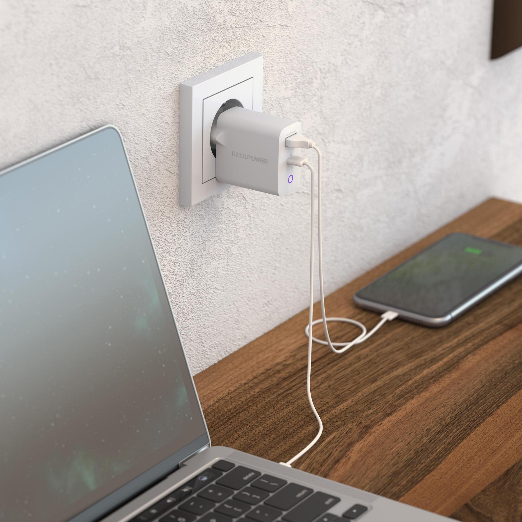 Laptop, Ladegerät in der Wand, Telefon wird auf dem Schreibtisch geladen. Holzoberfläche, weiße Wand.
