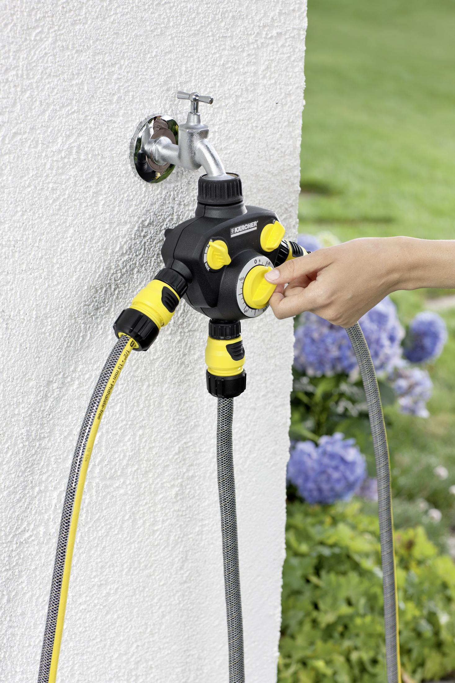 Eine Person stellt einen schwarz-gelben Gartenbewässerungstimer ein, der an einen Wasserhahn angeschlossen ist.