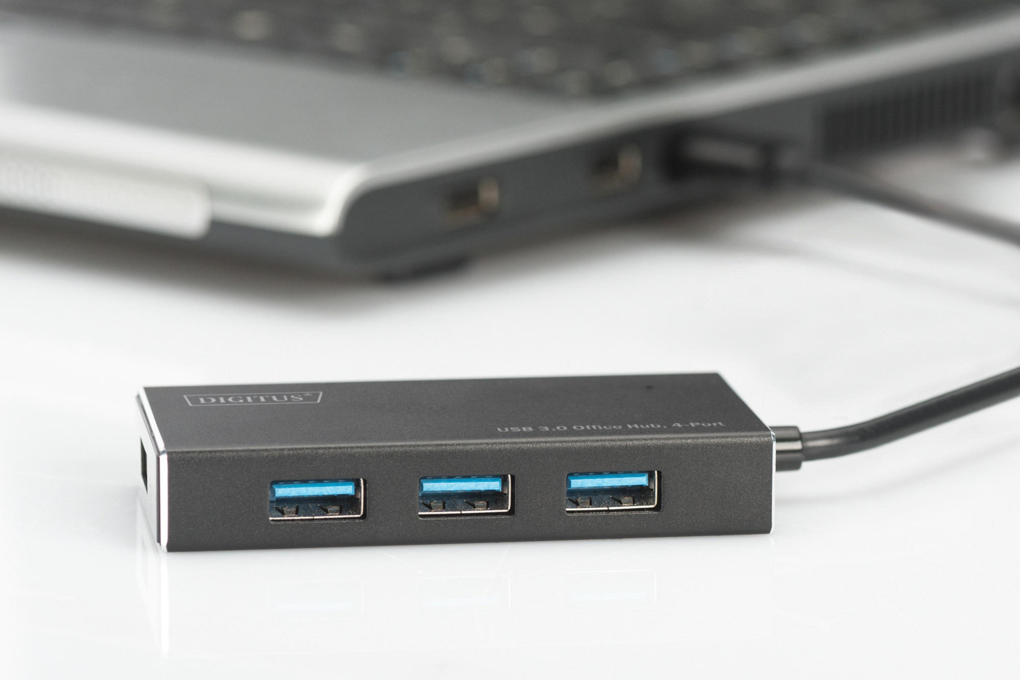 Ein USB-Hub mit drei blauen USB-Anschlüssen, der an einem Laptop auf einer weißen Oberfläche angeschlossen ist.
