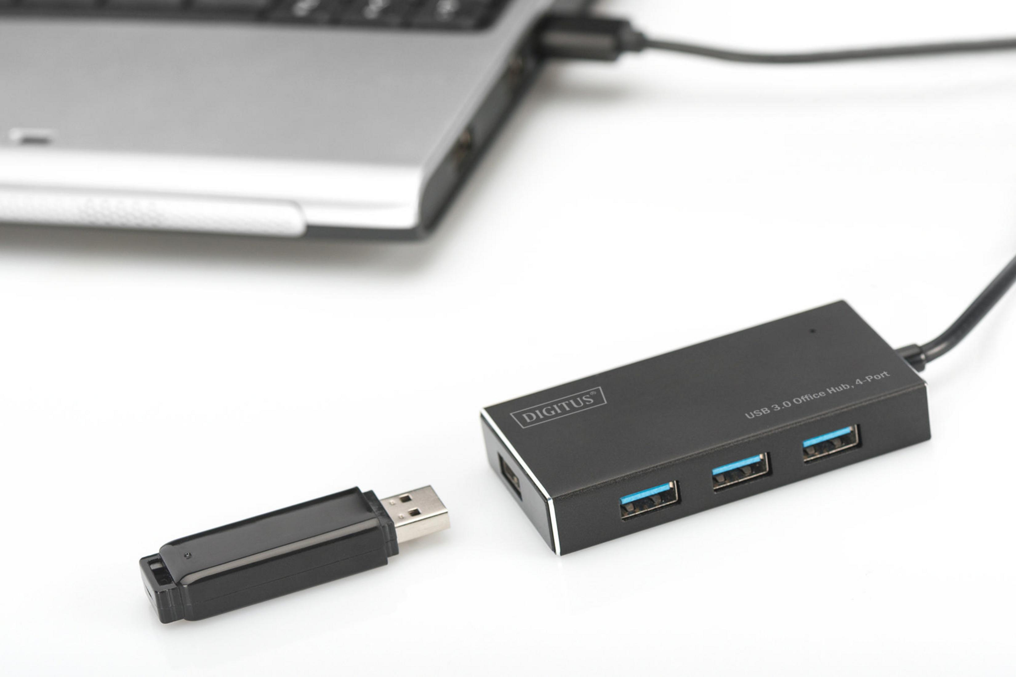 Schwarzer USB-Hub mit Laptop verbunden, USB-Stick daneben auf weißer Oberfläche.