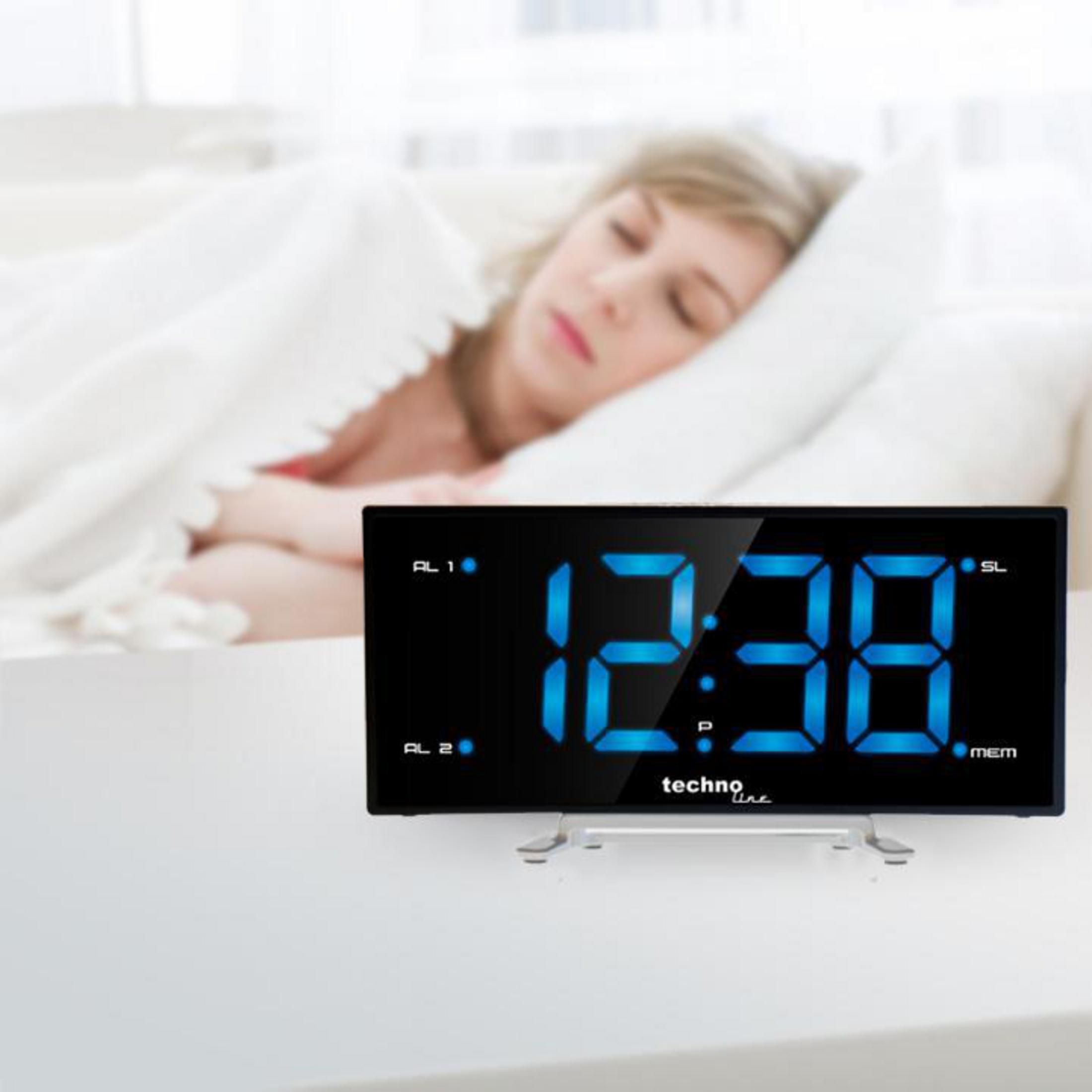 Digitaluhr mit blauen Ziffern, die 12:38 anzeigt, und eine schlafende Frau im Hintergrund.