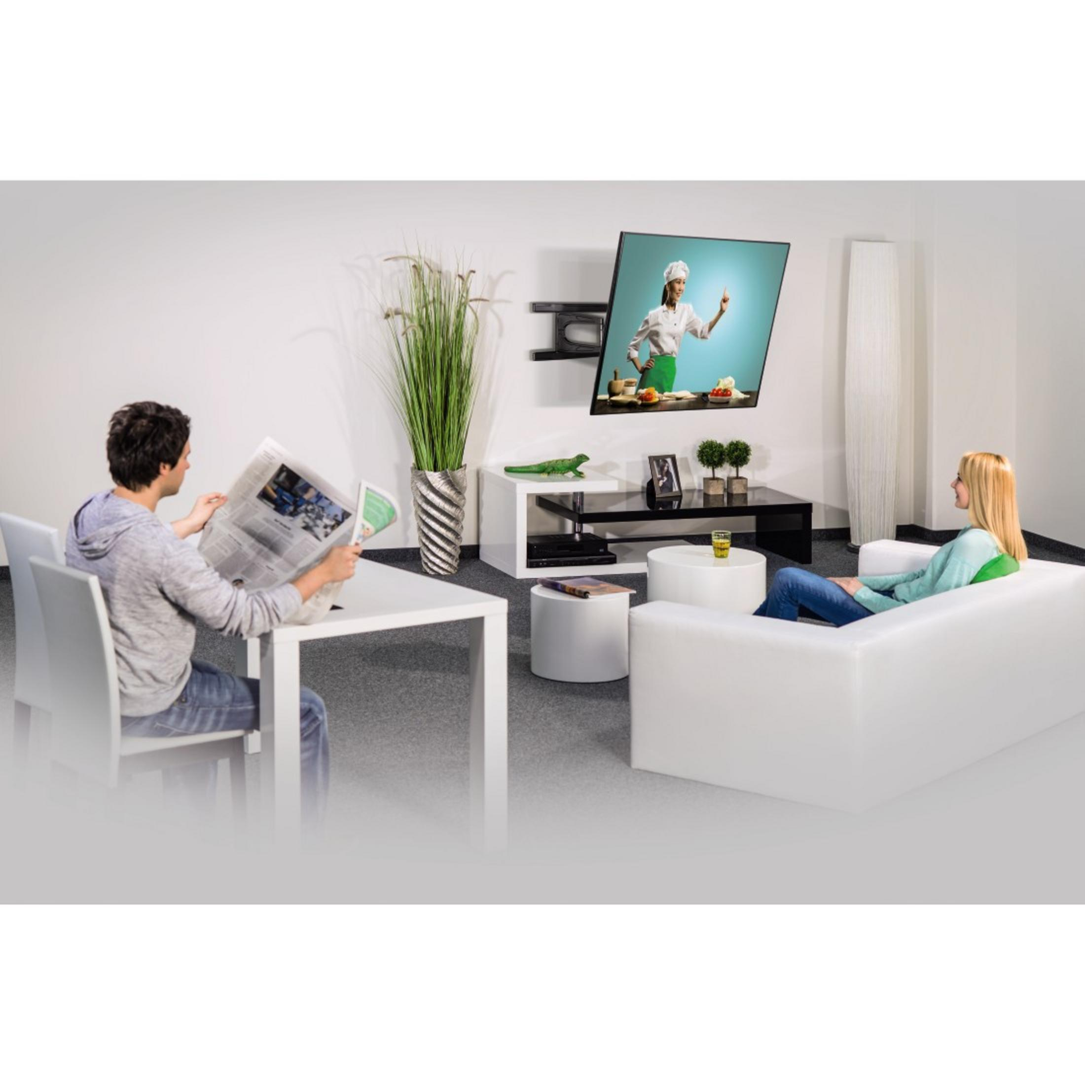 Wohnzimmer mit Fernseher, Sofa und zwei Personen. Einer liest Zeitung, der andere auf dem Sofa.