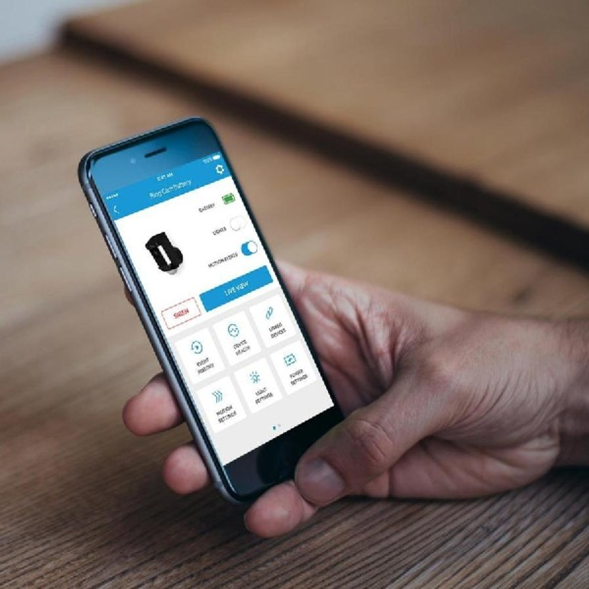 Ręka trzymająca smartfon z interfejsem aplikacji inteligentnego domu na drewnianej powierzchni.