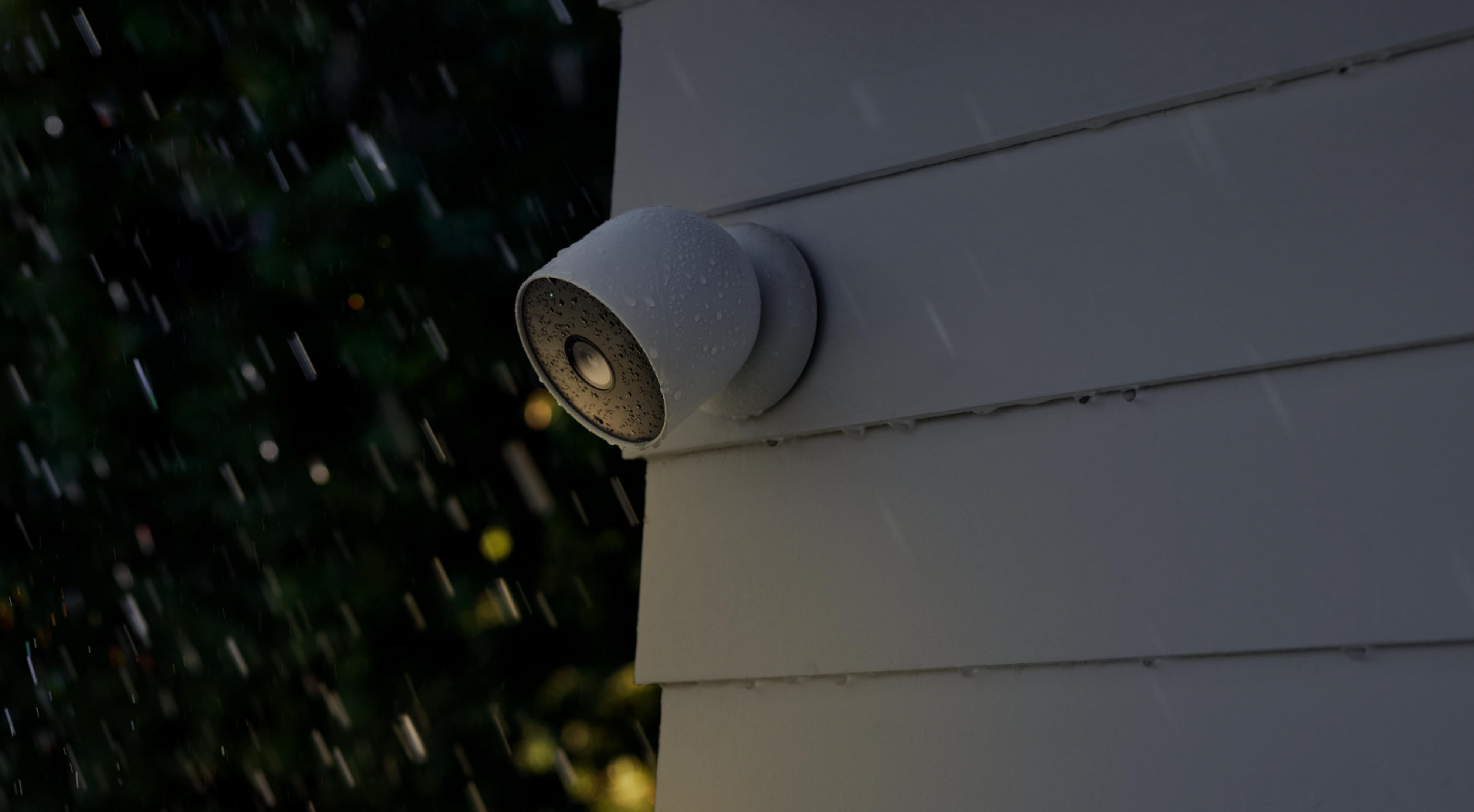 Biała kamera bezpieczeństwa zamontowana na zewnętrznej ścianie domu, pada deszcz.