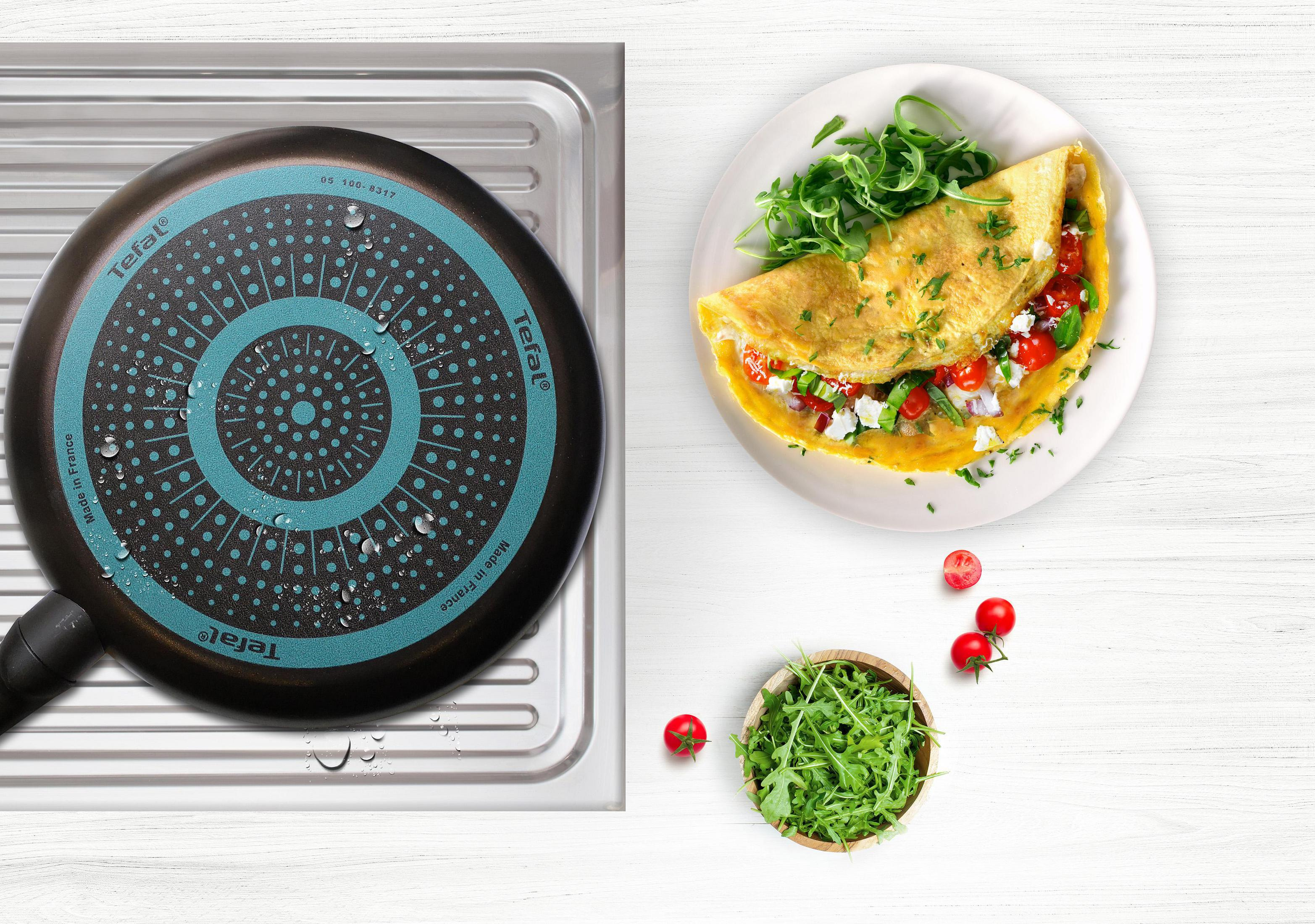 Omlet i patelnia. Patelnia ma czarną powierzchnię i turkusowy wzór. Omlet ma sałatę.