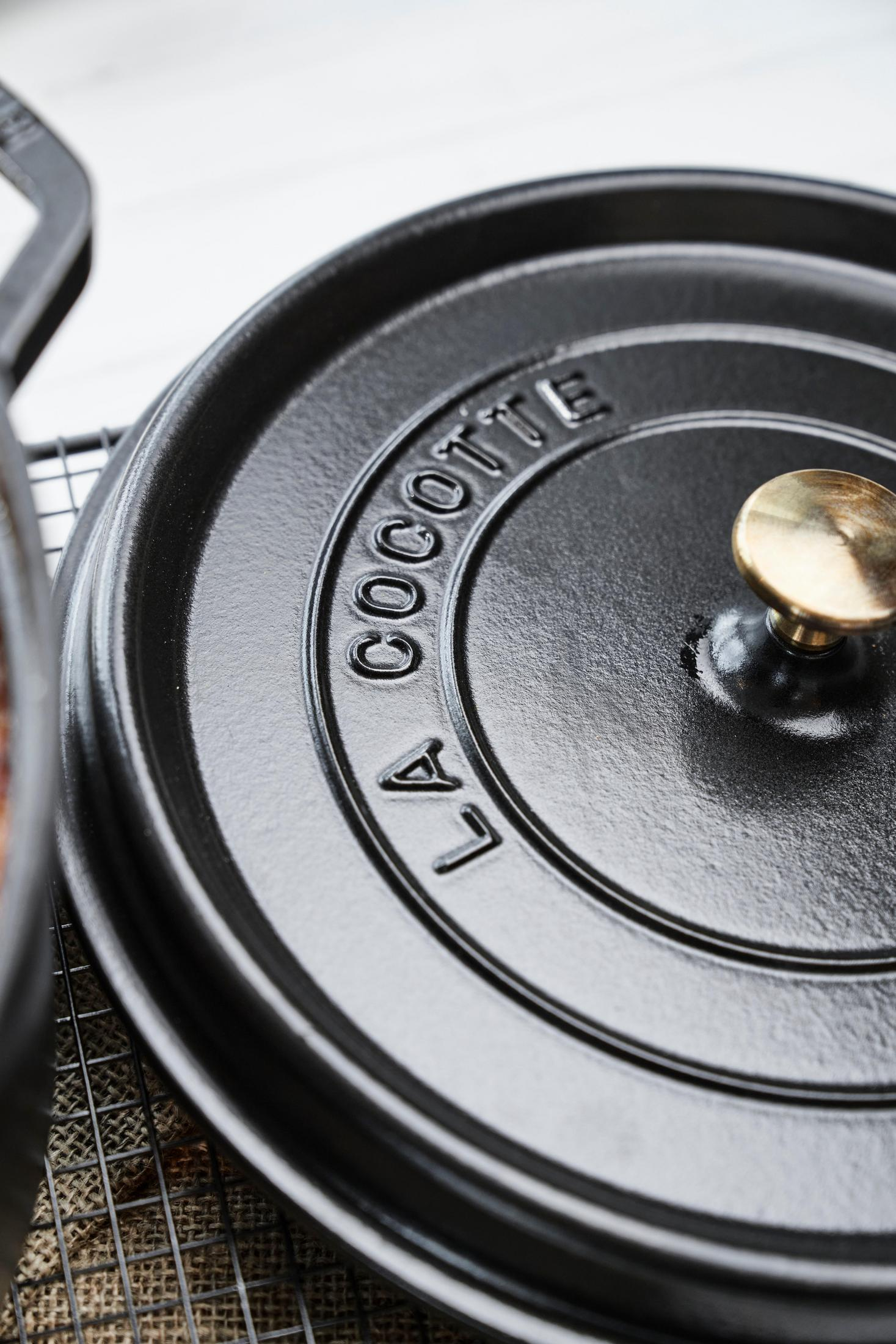 Couvercle de casserole noir avec bouton doré, le mot LA COCOTTE est visible.