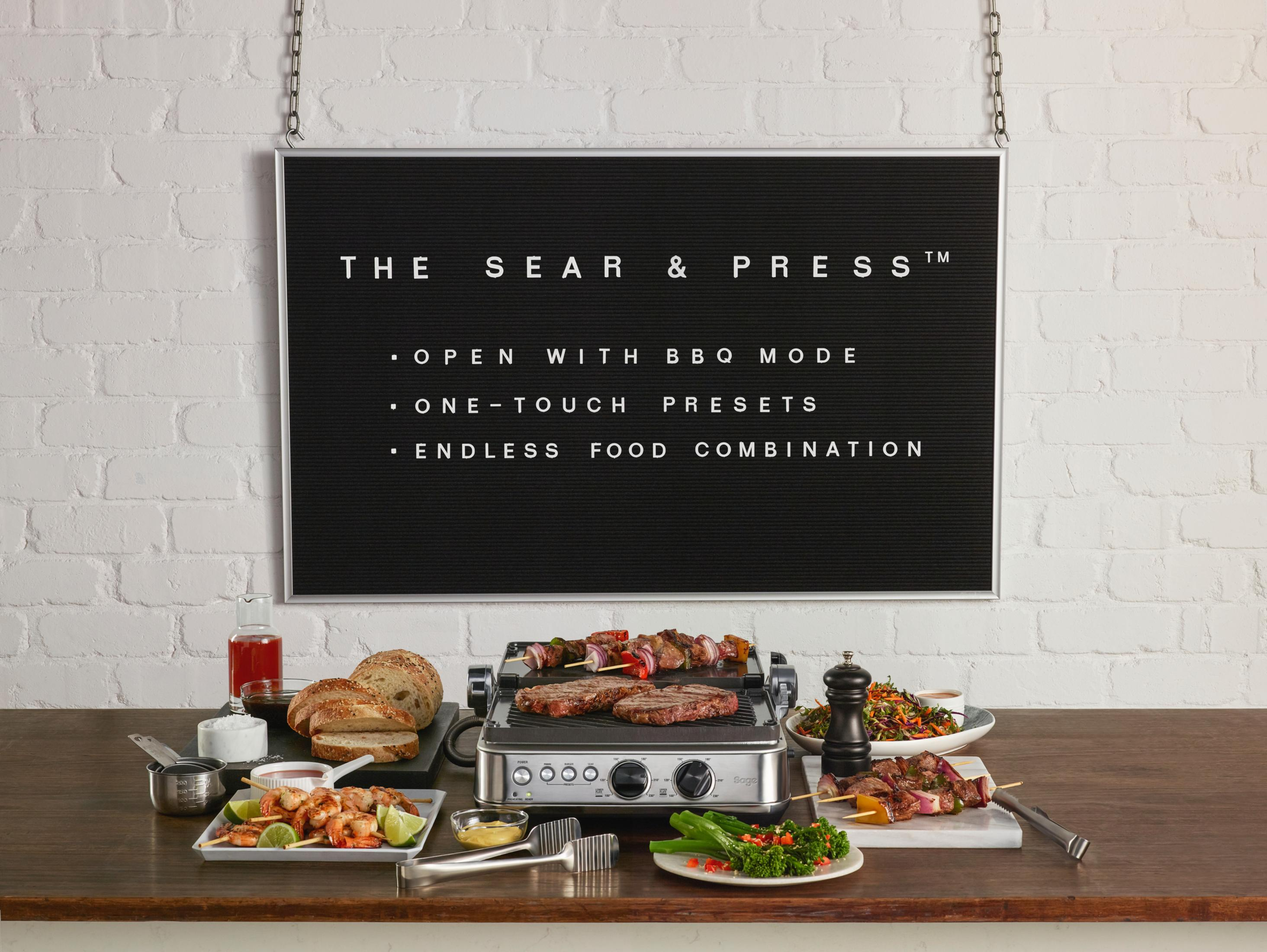 Grill z jedzeniem na nim i talerzami z jedzeniem wokół. Znak mówi 'The Sear & Press'.