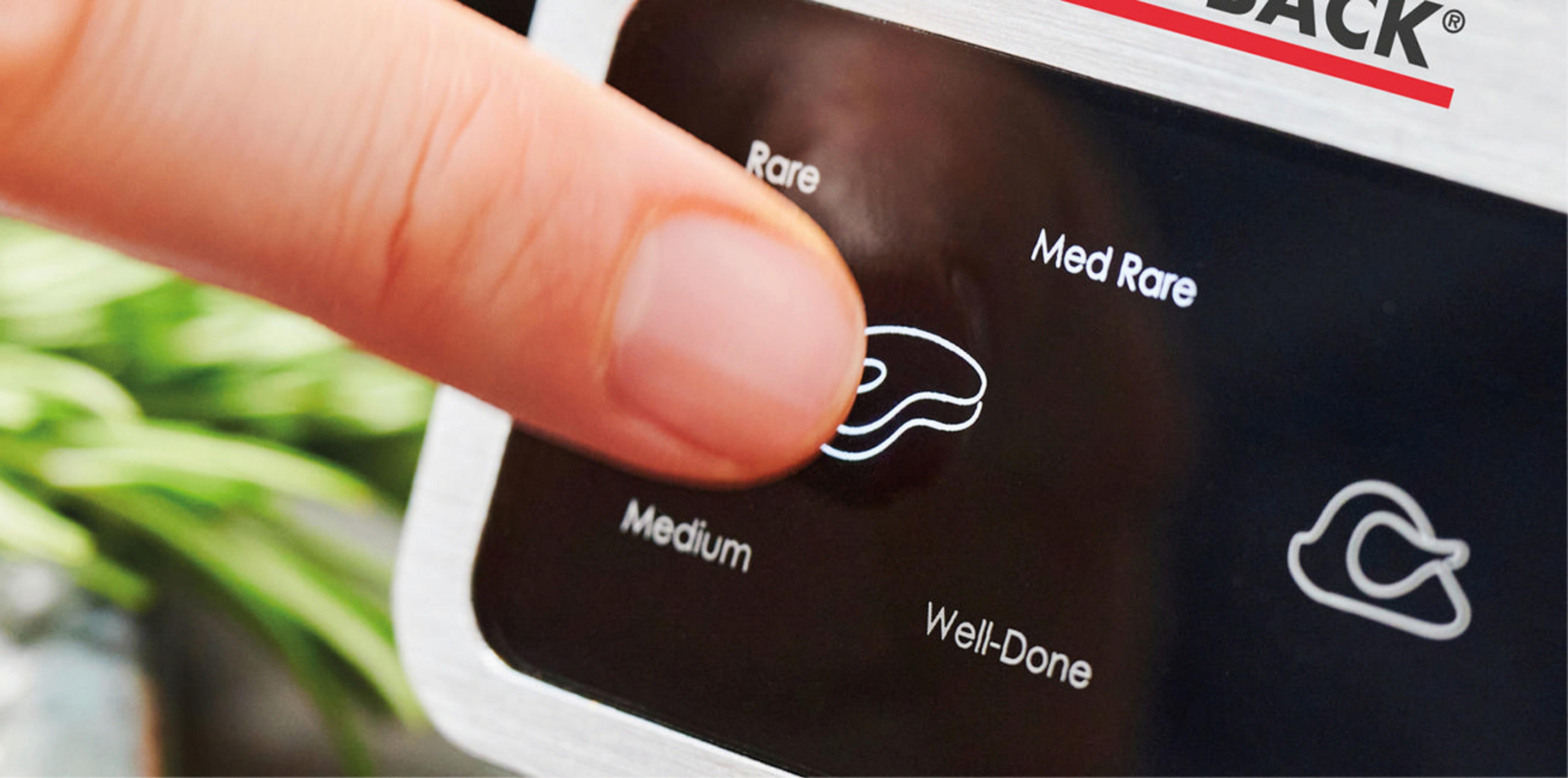 Un doigt appuie sur l'icône du steak pour 'Medium' sur un appareil de cuisson. Autres options.