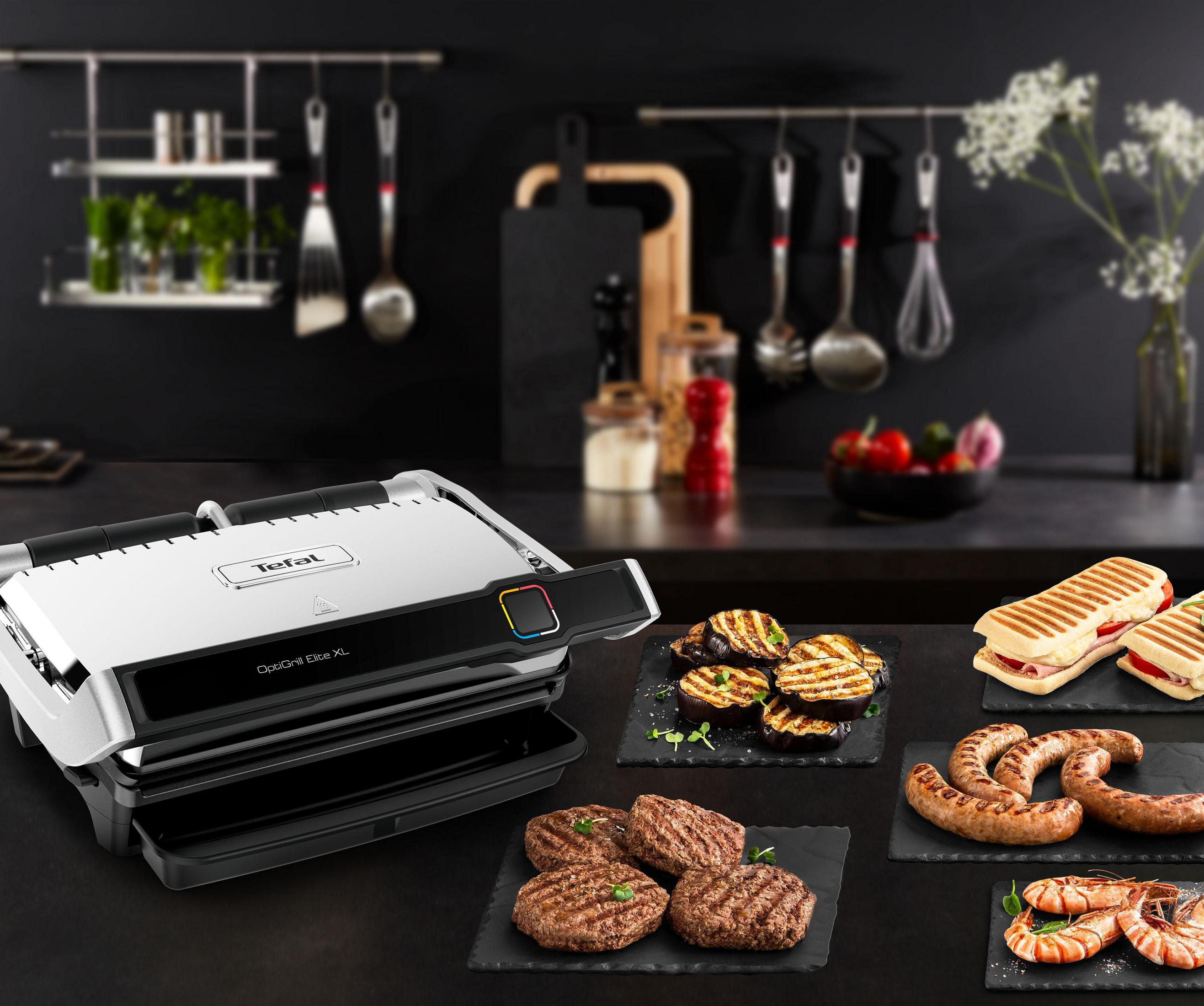 Tefal OptiGrill XL z grillowanymi potrawami. Zawiera burgery, kiełbaski, bakłażany i kanapki na talerzach.