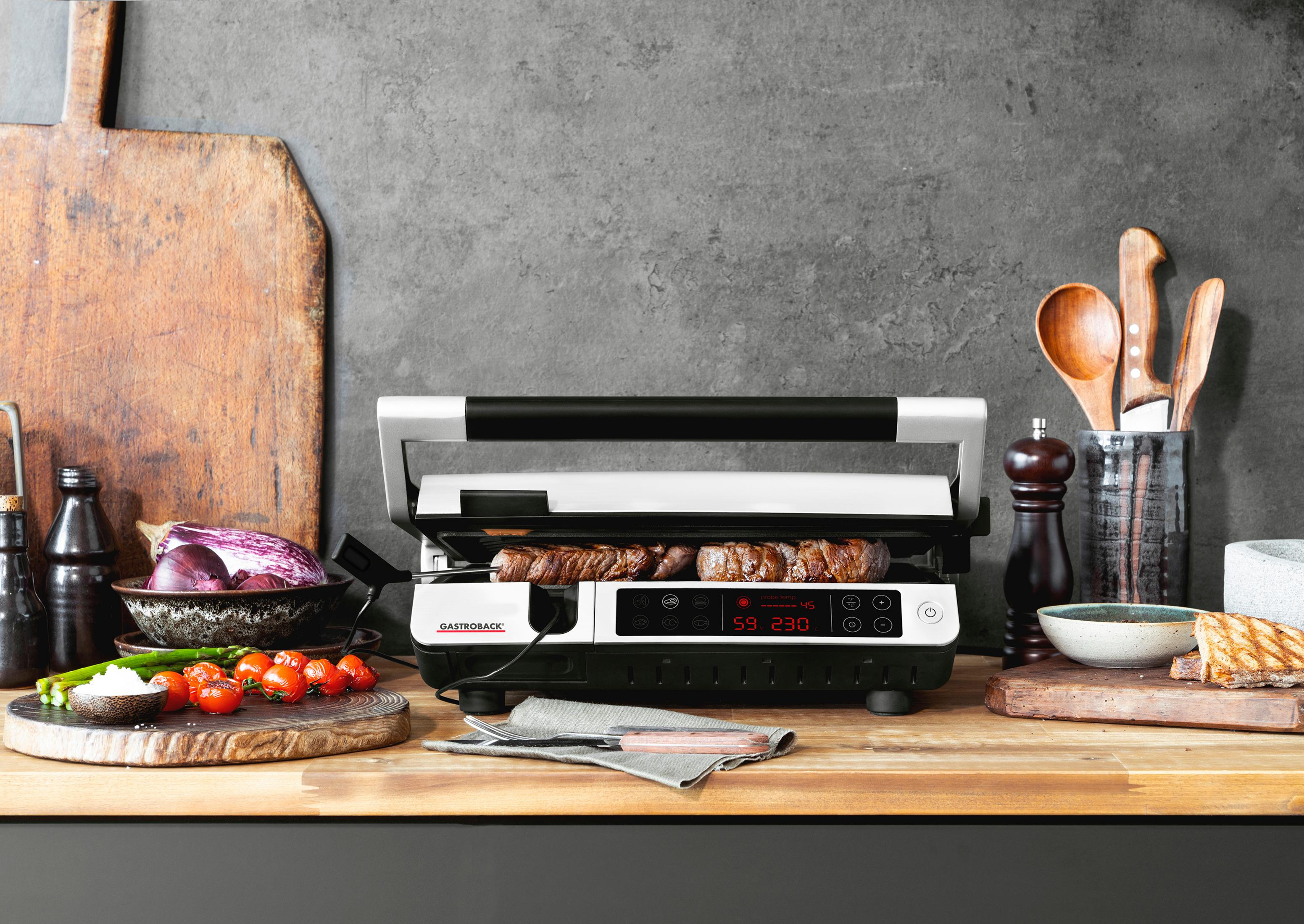 Grill z jedzeniem. Drewniane deski do krojenia ze składnikami z boku. Szare tło.