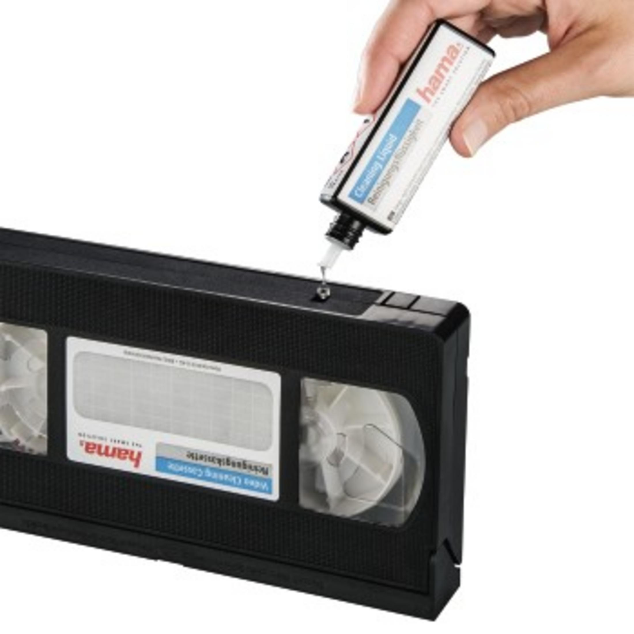 Hand gießt Reinigungsflüssigkeit auf eine schwarze VHS-Kassette, weißer Hintergrund.