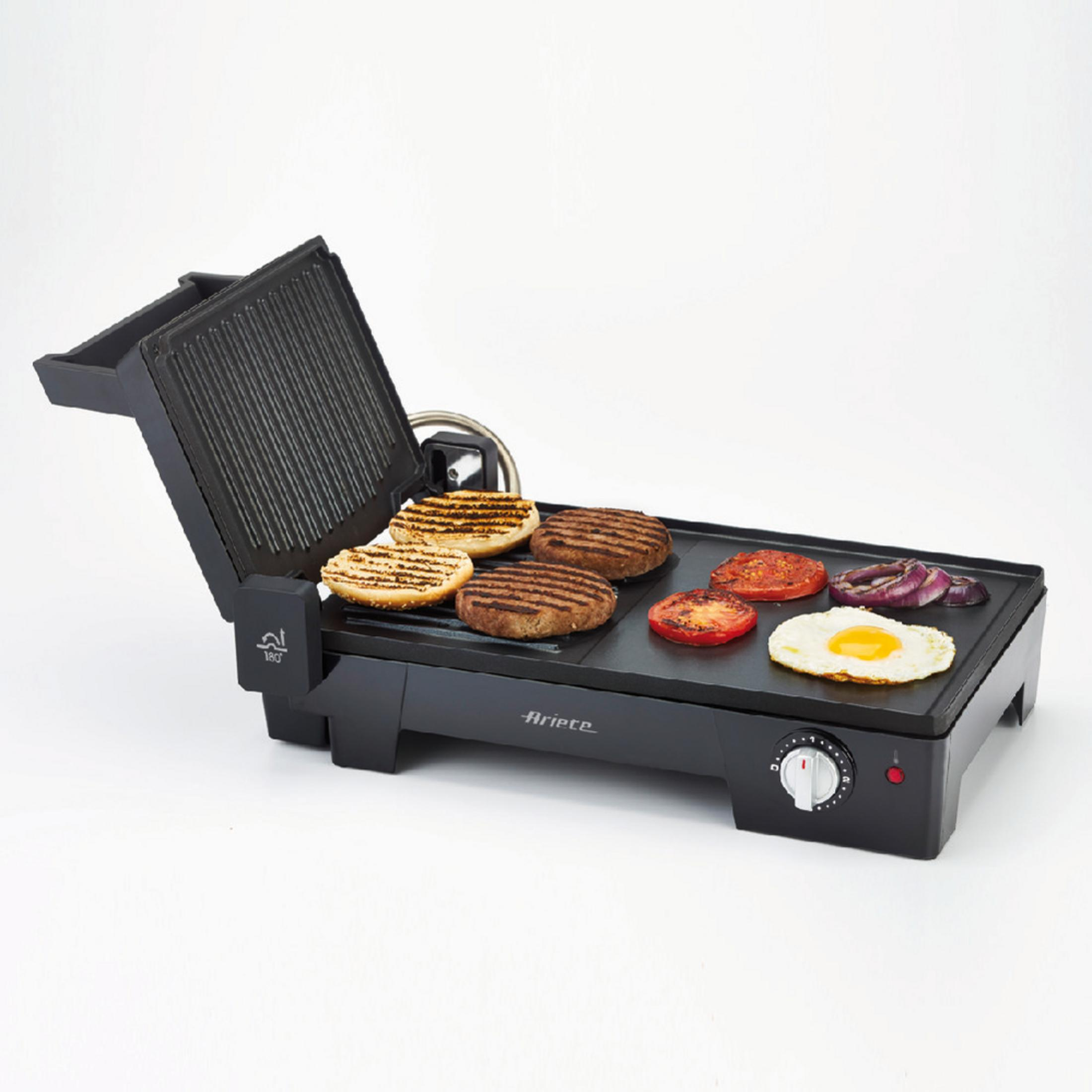 Black grill with food on it: burgers, tomatoes, eggs, and onions.