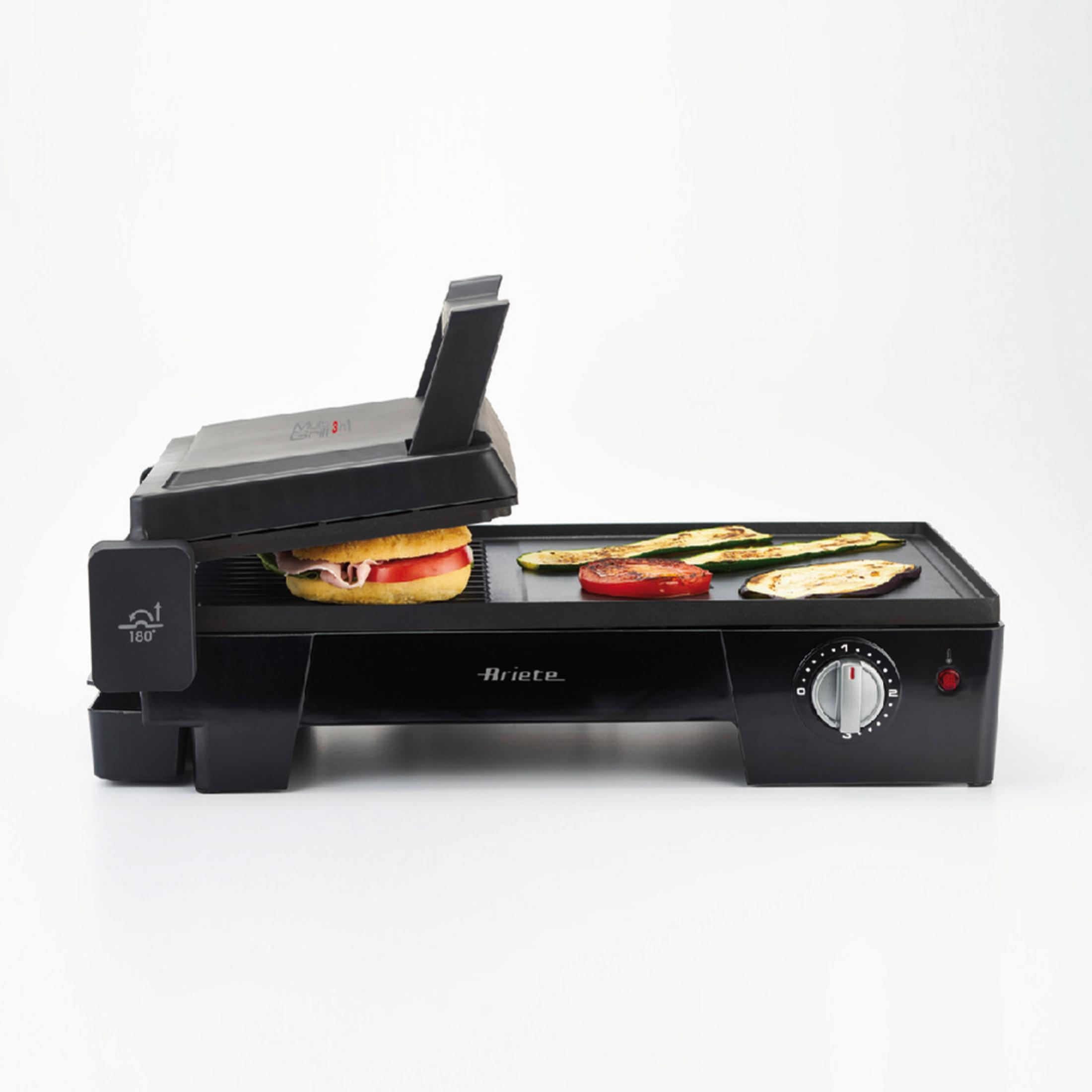 A black sandwich grill with food inside and vegetables on the grilling surface.