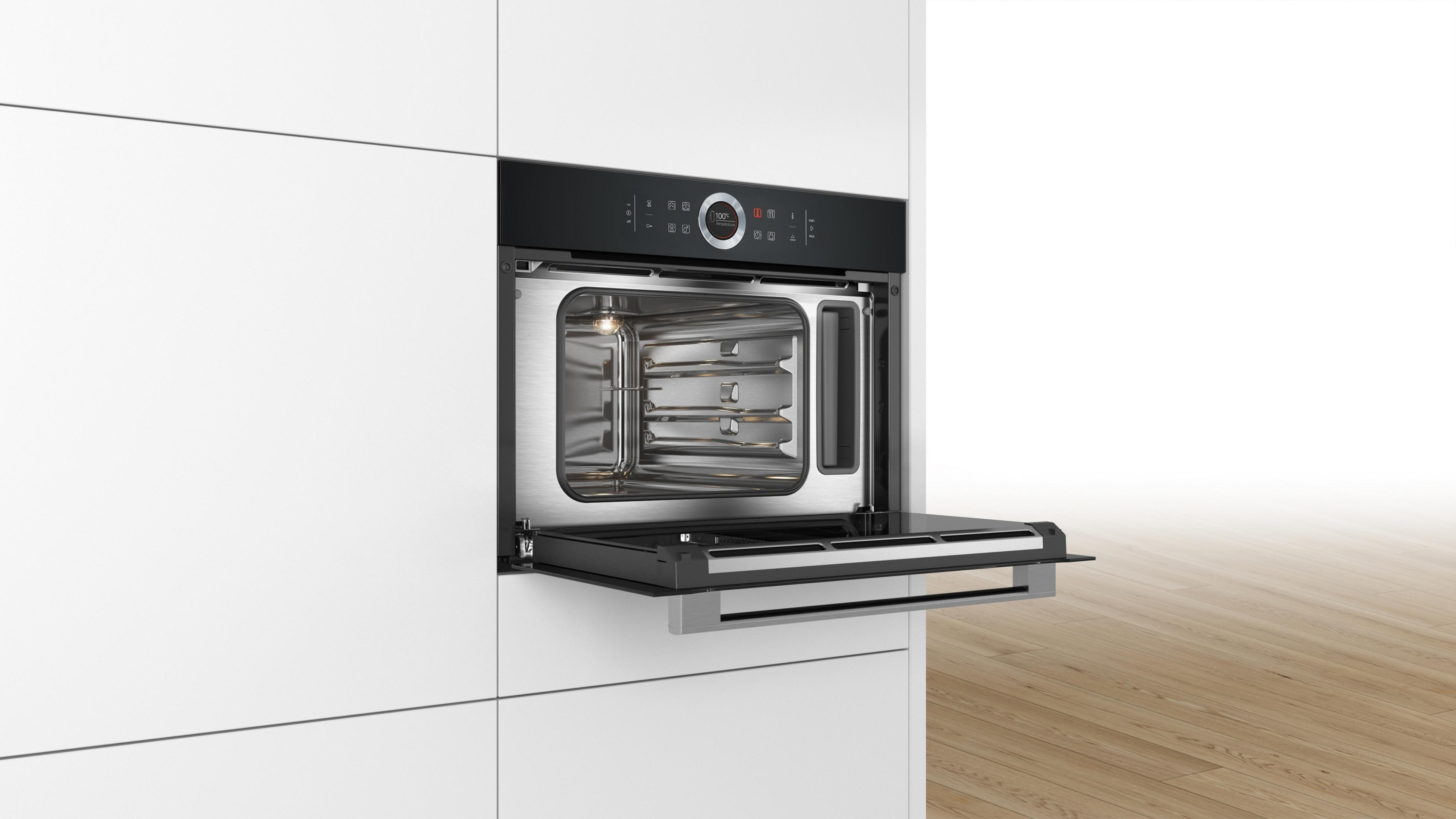 Ingebouwde zwarte oven met open deur, op witte muur en houten vloer.