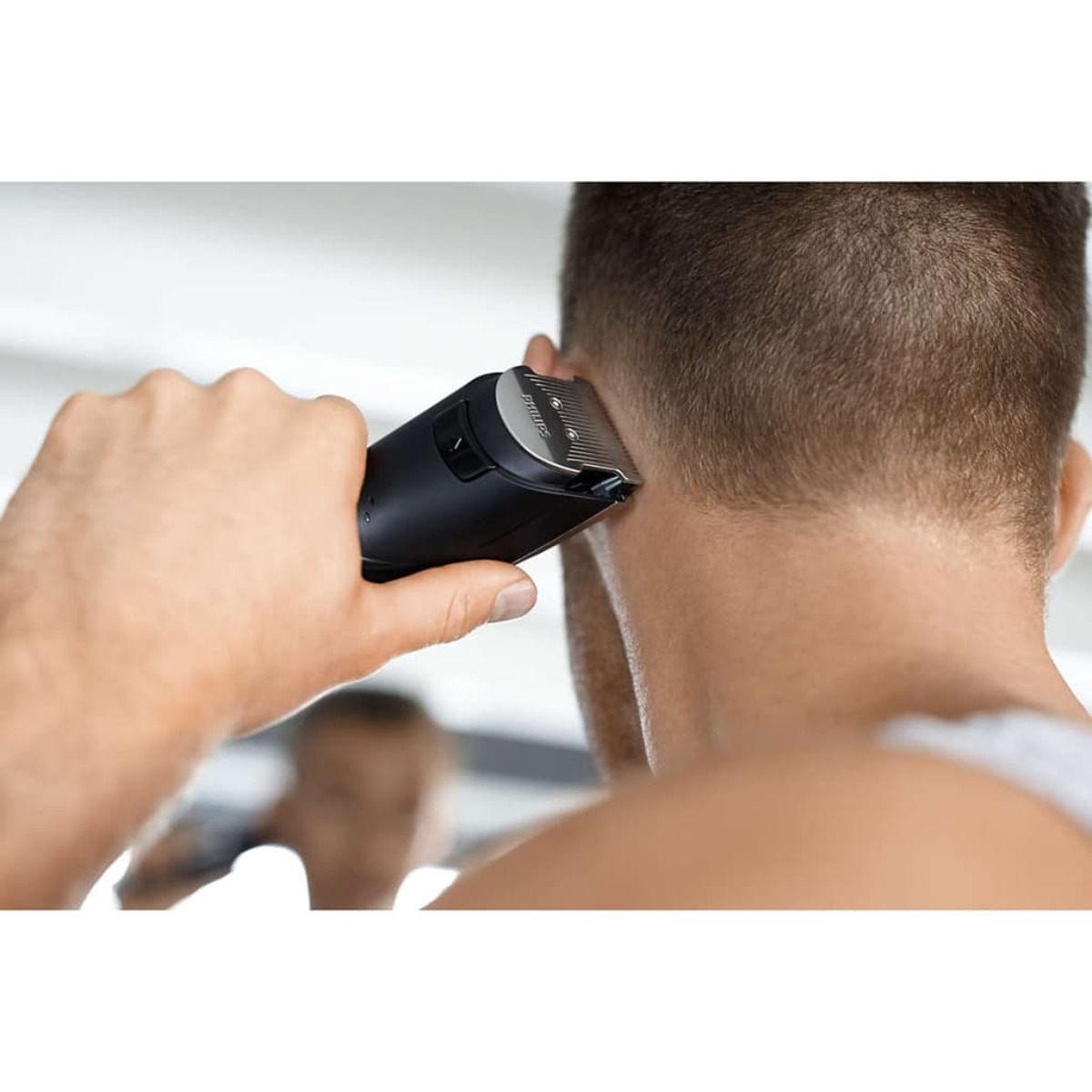 Un hombre usando una cortadora de cabello negra para recortar su cabello, espejo en el fondo.