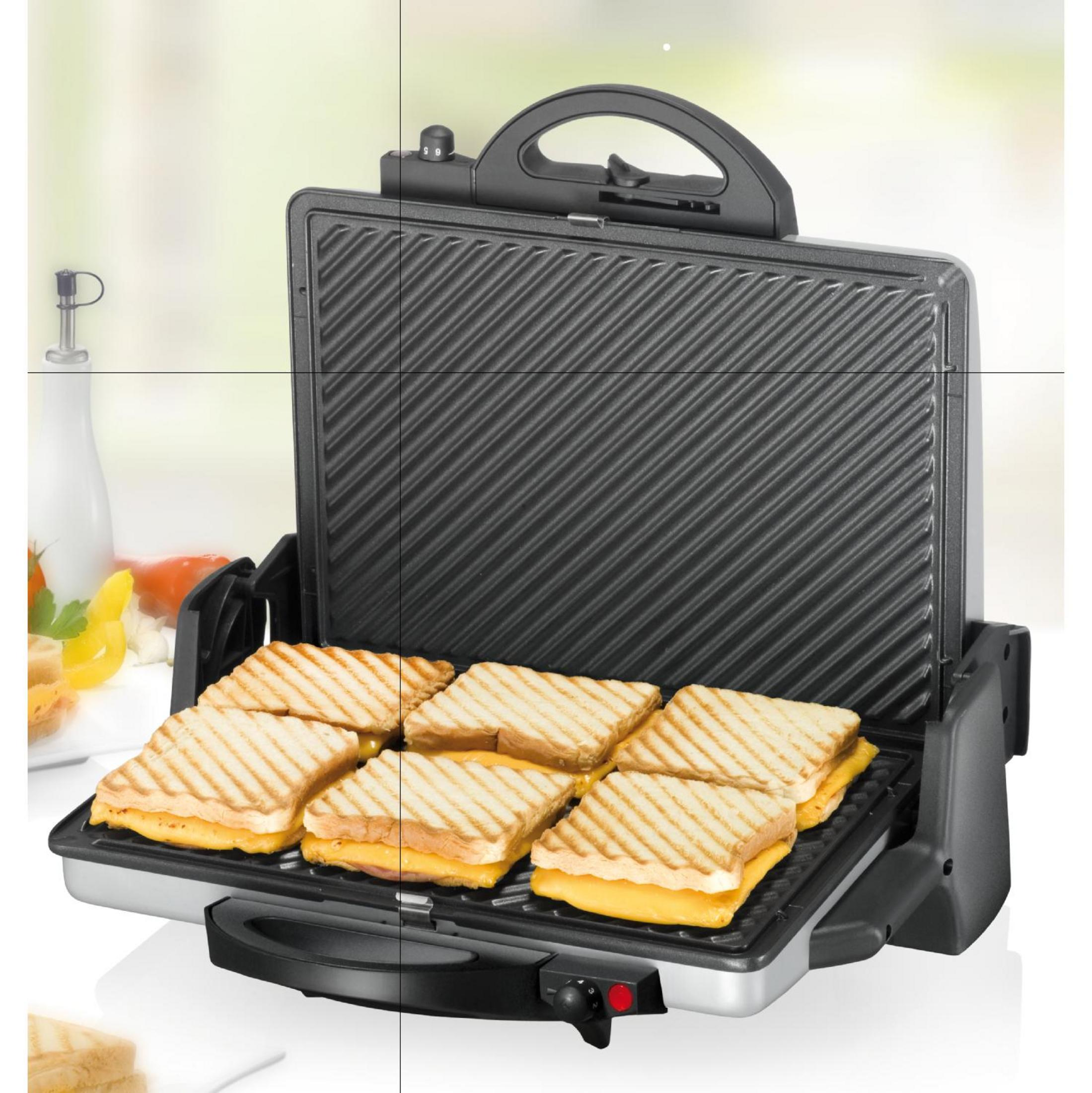 Sandwich maker aperto con sei panini tostati. La sandwich maker è argentata e nera.