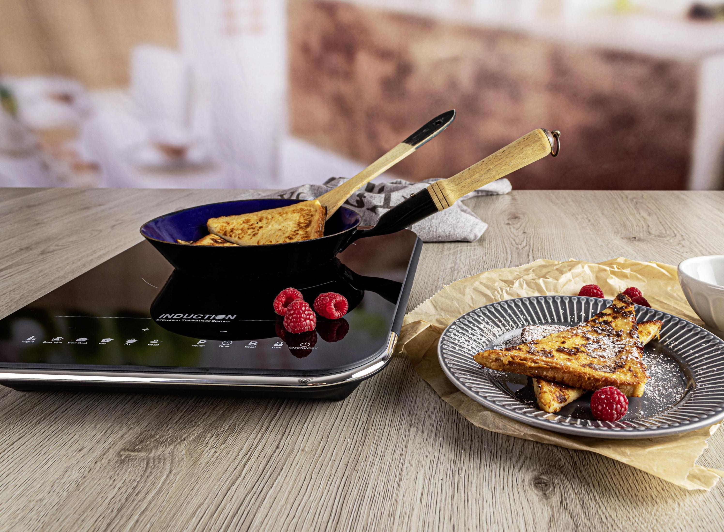 Tosty francuskie na patelni i na talerzu z malinami. Drewniany stół.