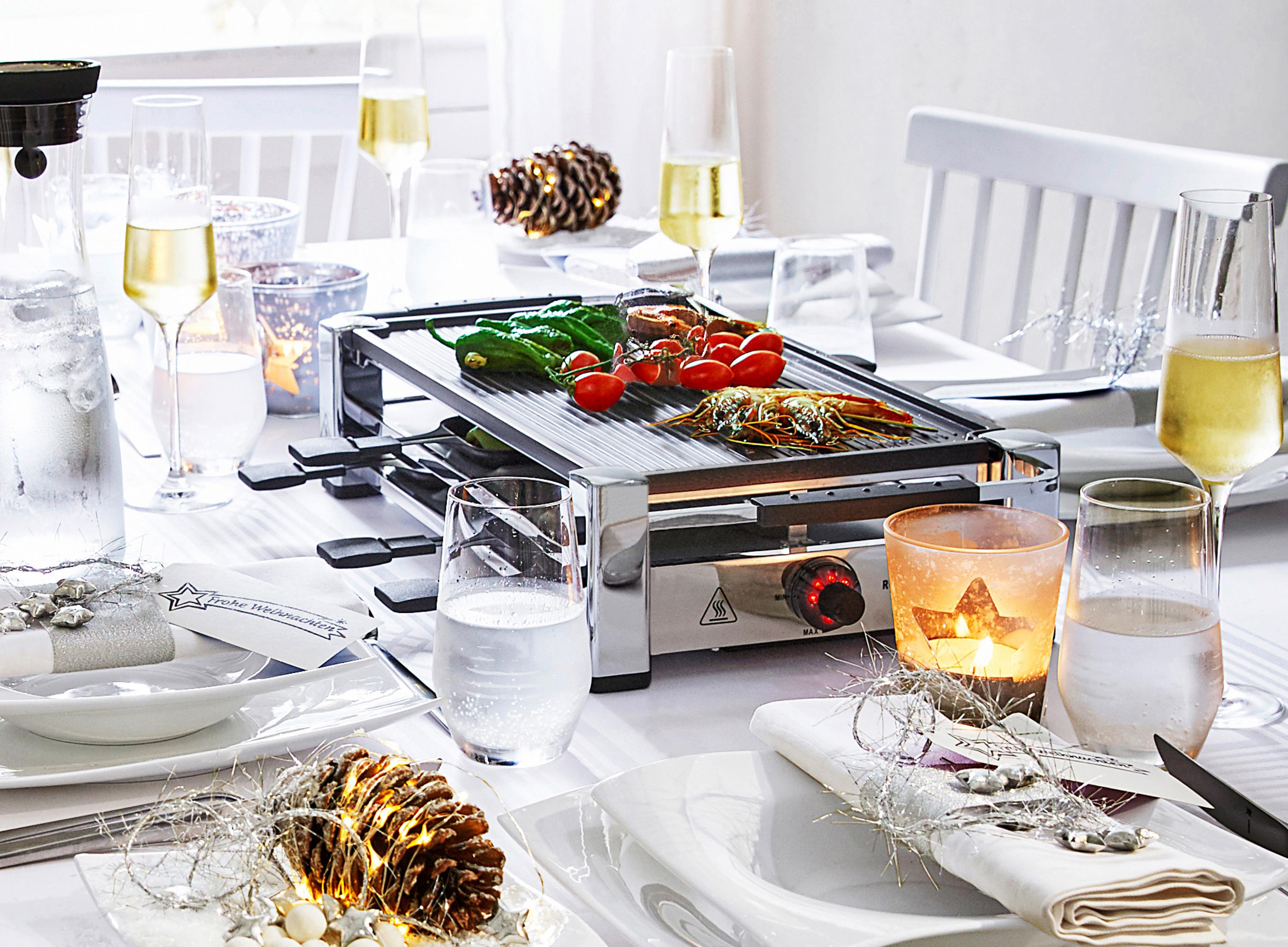 Stół nakryty do posiłku z grillem do raclette, jedzeniem, napojami i świecami.