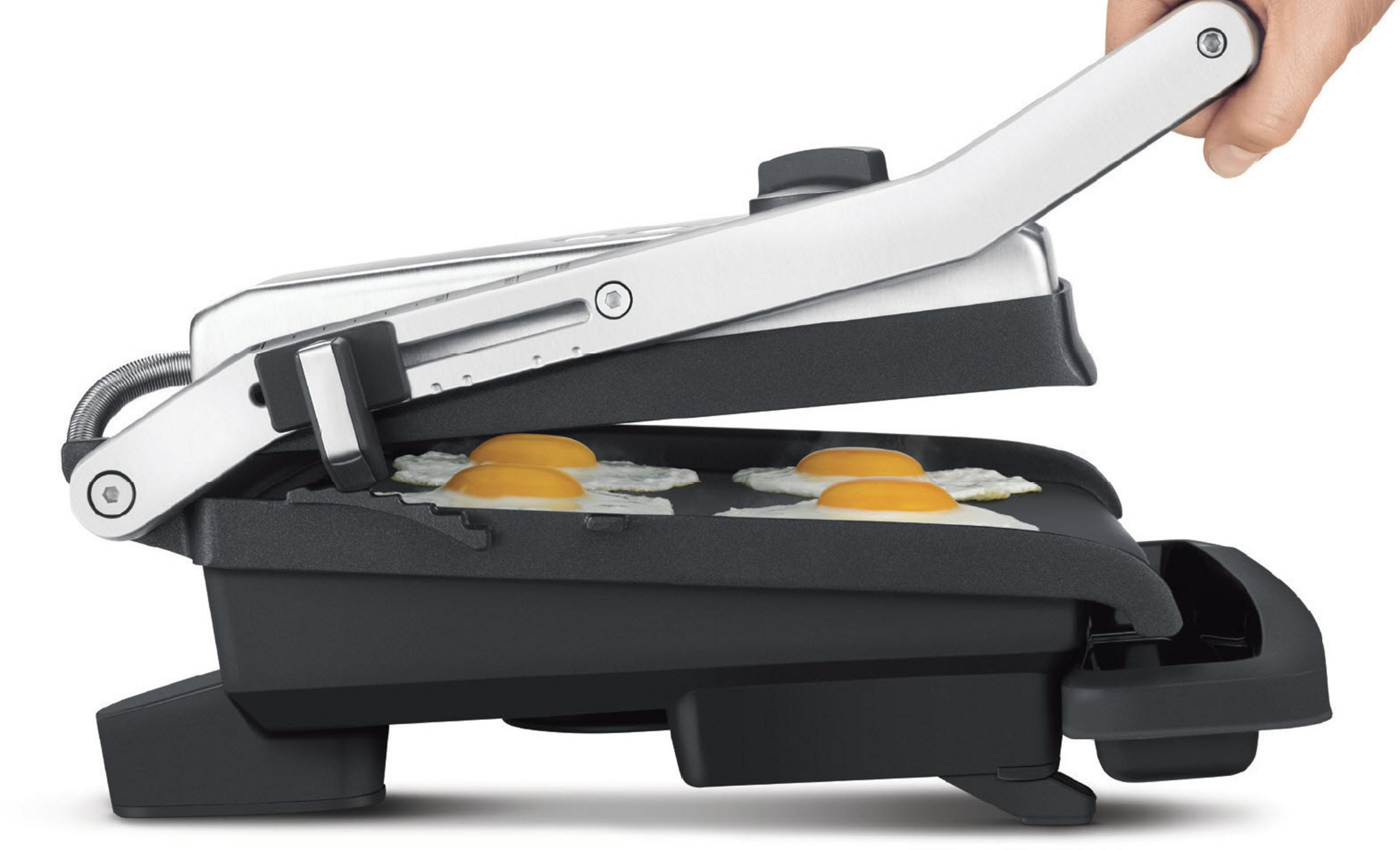 Grill z czterema jajkami sadzonymi. Ręka podnosi górę grilla. Czarny i srebrny.