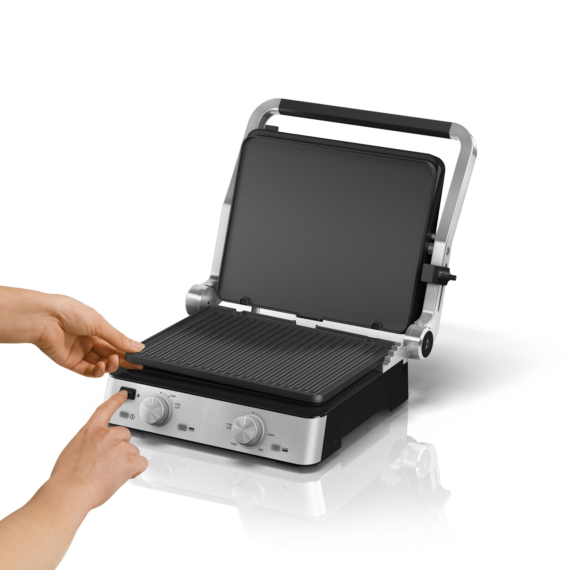 Silberner und schwarzer Panini-Grill, offen, mit einer Hand, die einen Knopf drückt. Weißer Hintergrund.