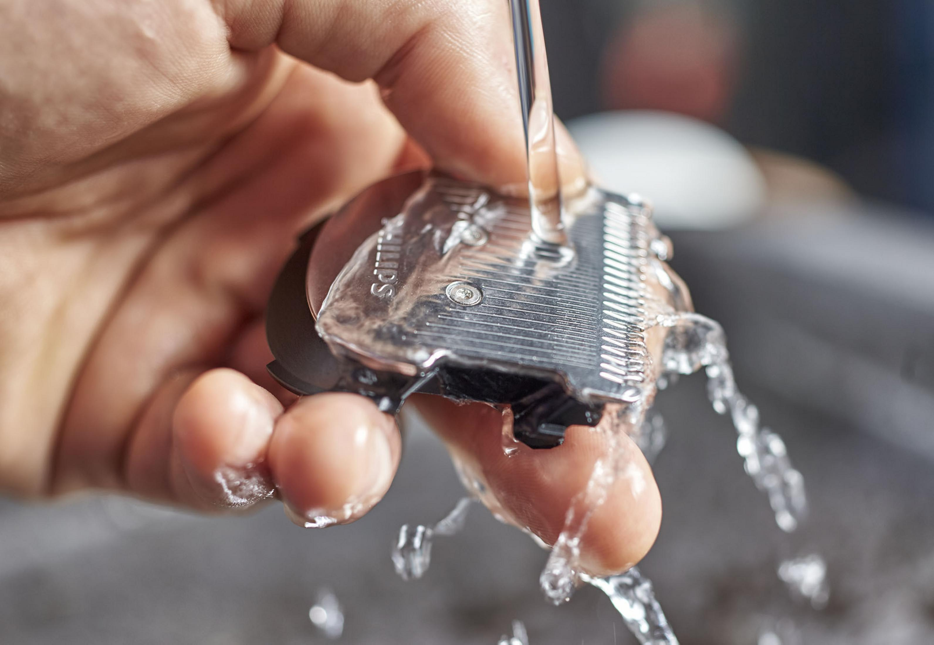 Mano enjuagando una cuchilla de cortapelos bajo agua corriente.