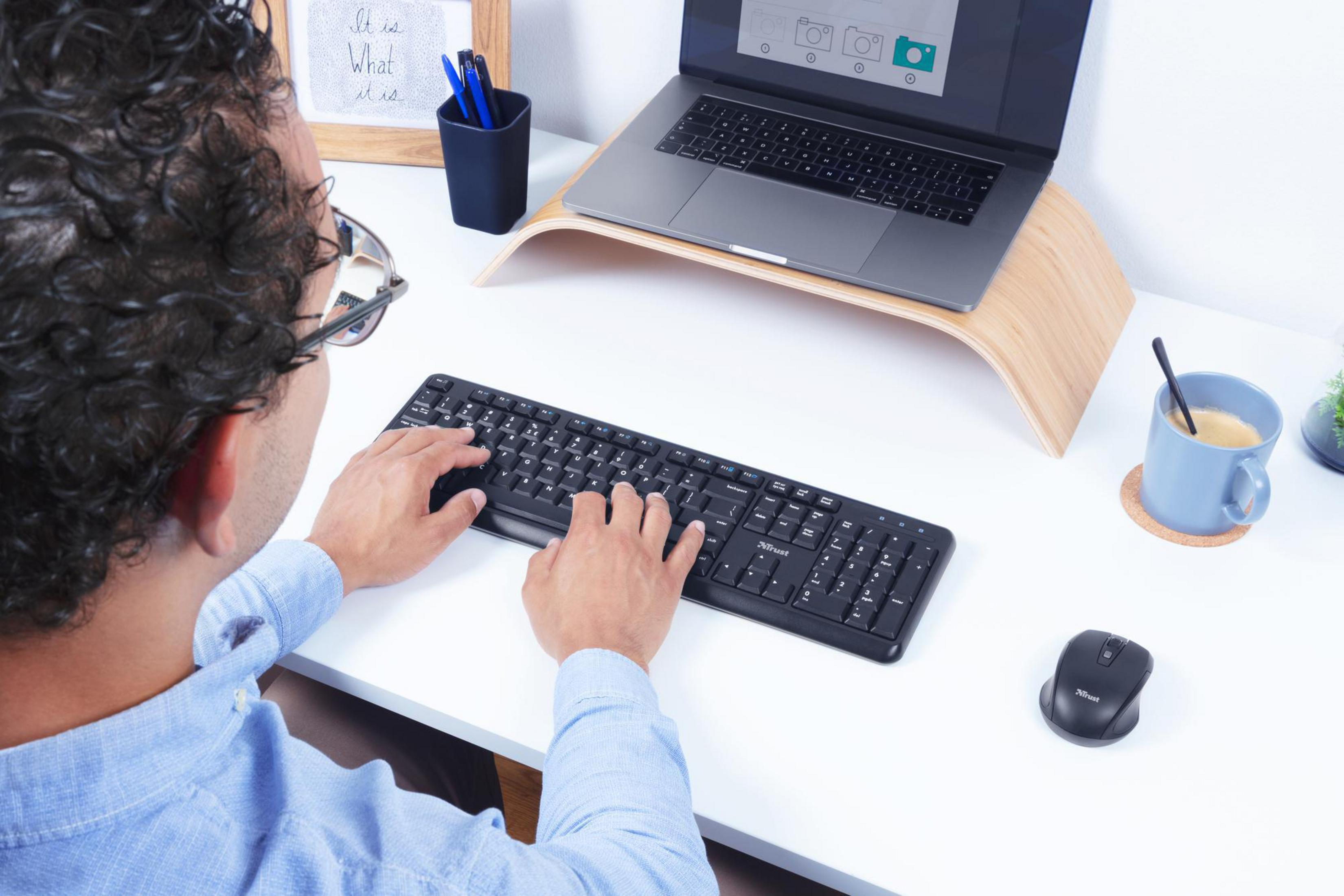 Un uomo al lavoro a una scrivania con un laptop su un supporto in legno e una tastiera.