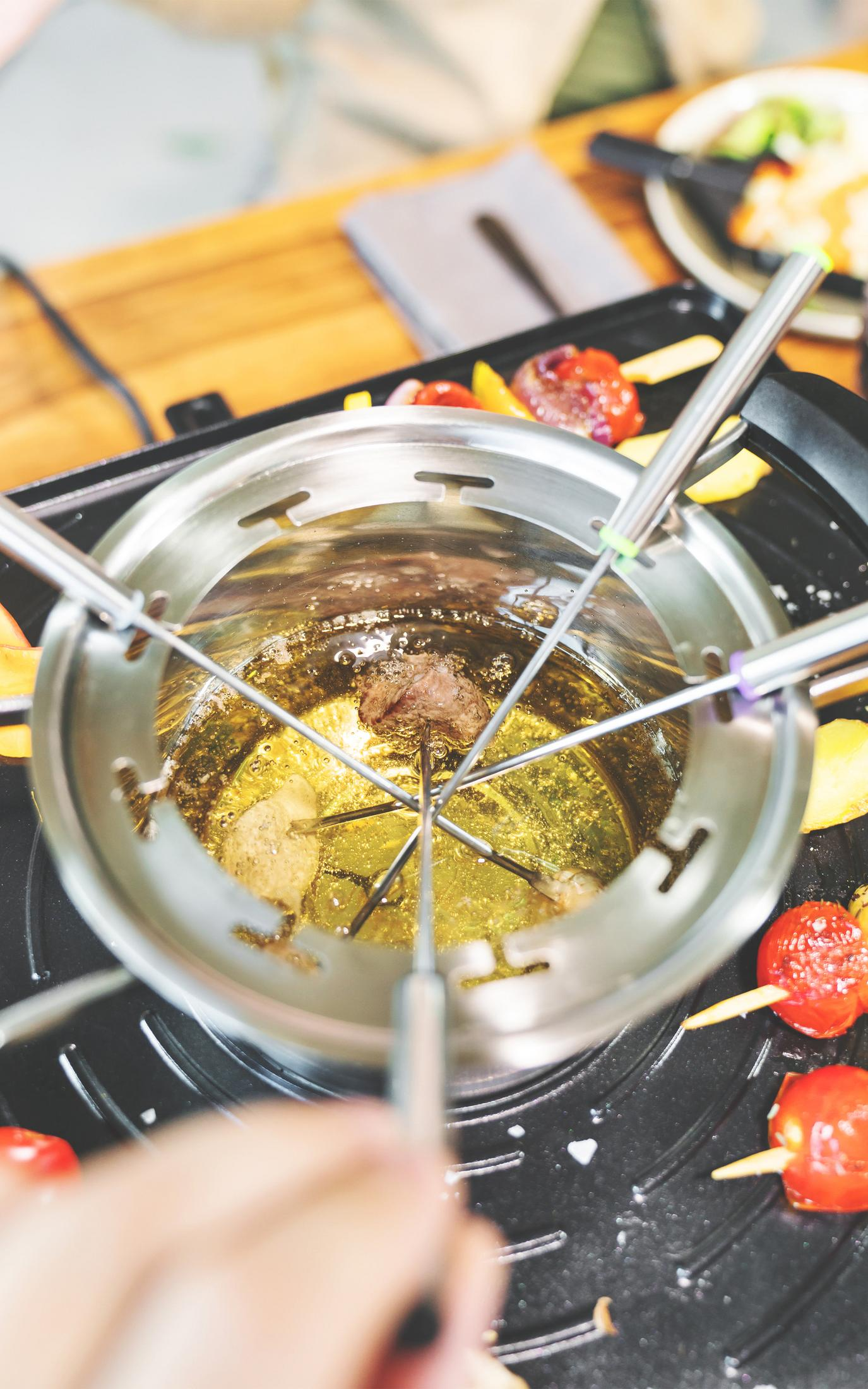 Una pentola per fondue con cibo su spiedini, parzialmente immersa nell'olio.