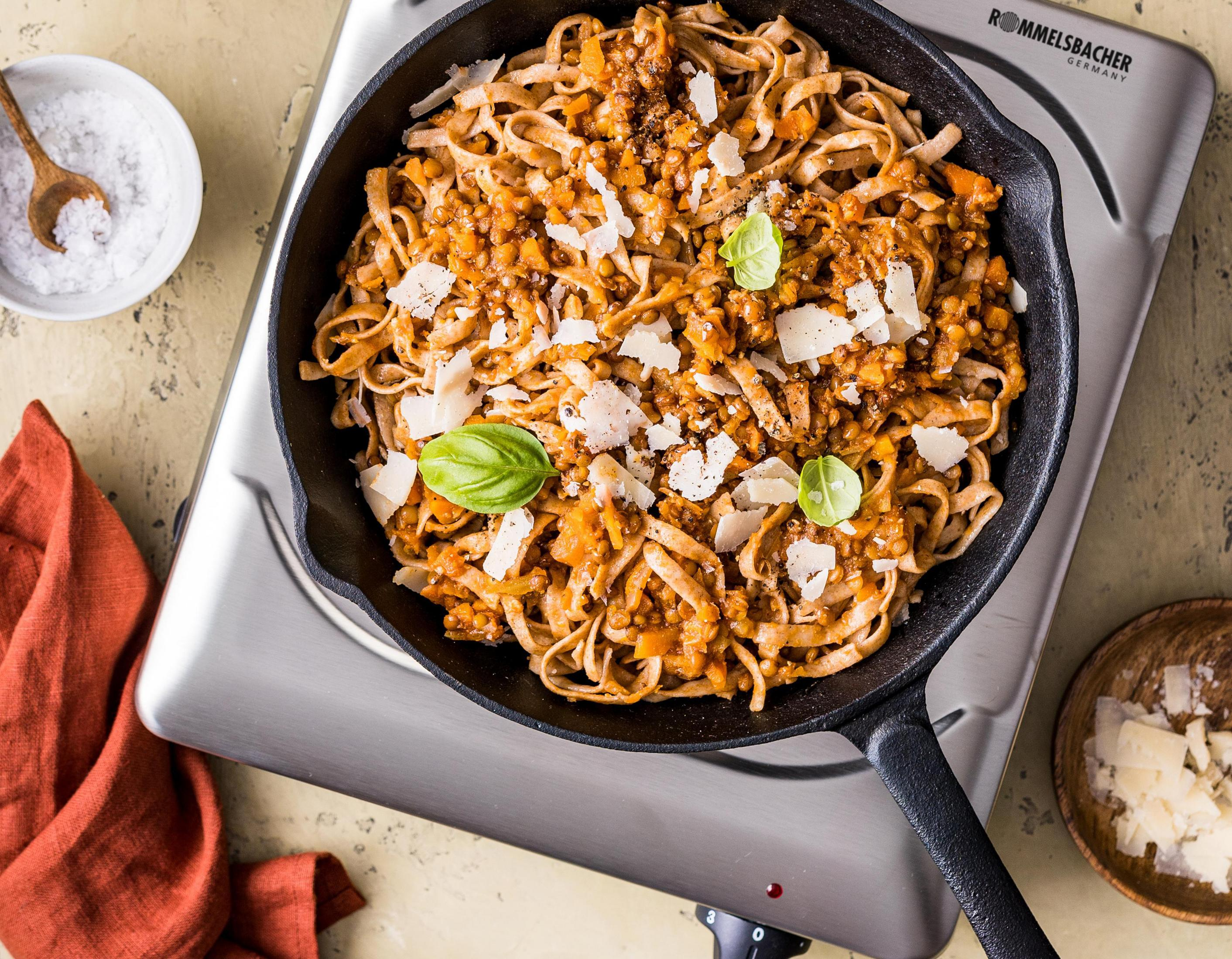 Padella in ghisa con pasta e salsa di pomodoro, guarnita con parmigiano e basilico.