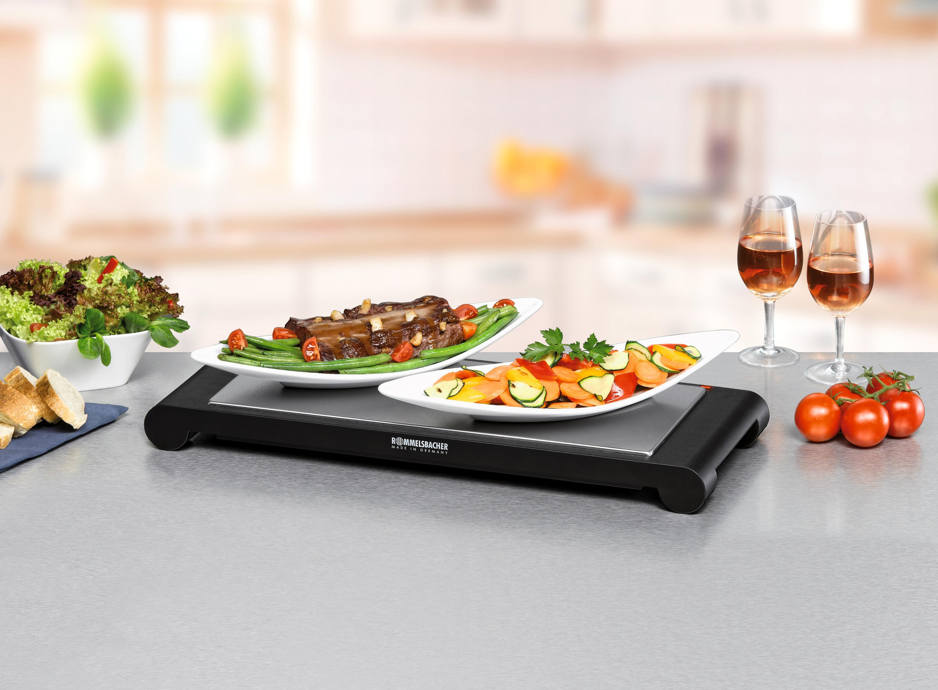 Ein Warmhalteblech mit zwei Tellern mit Essen, Weingläsern und Tomaten auf einem Tisch.
