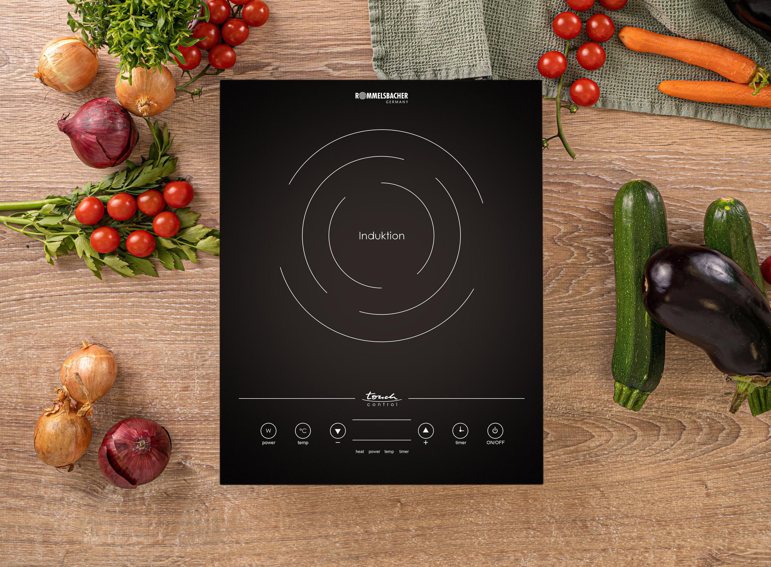 Czarna płyta indukcyjna otoczona warzywami na drewnianej powierzchni. Panel dotykowy.