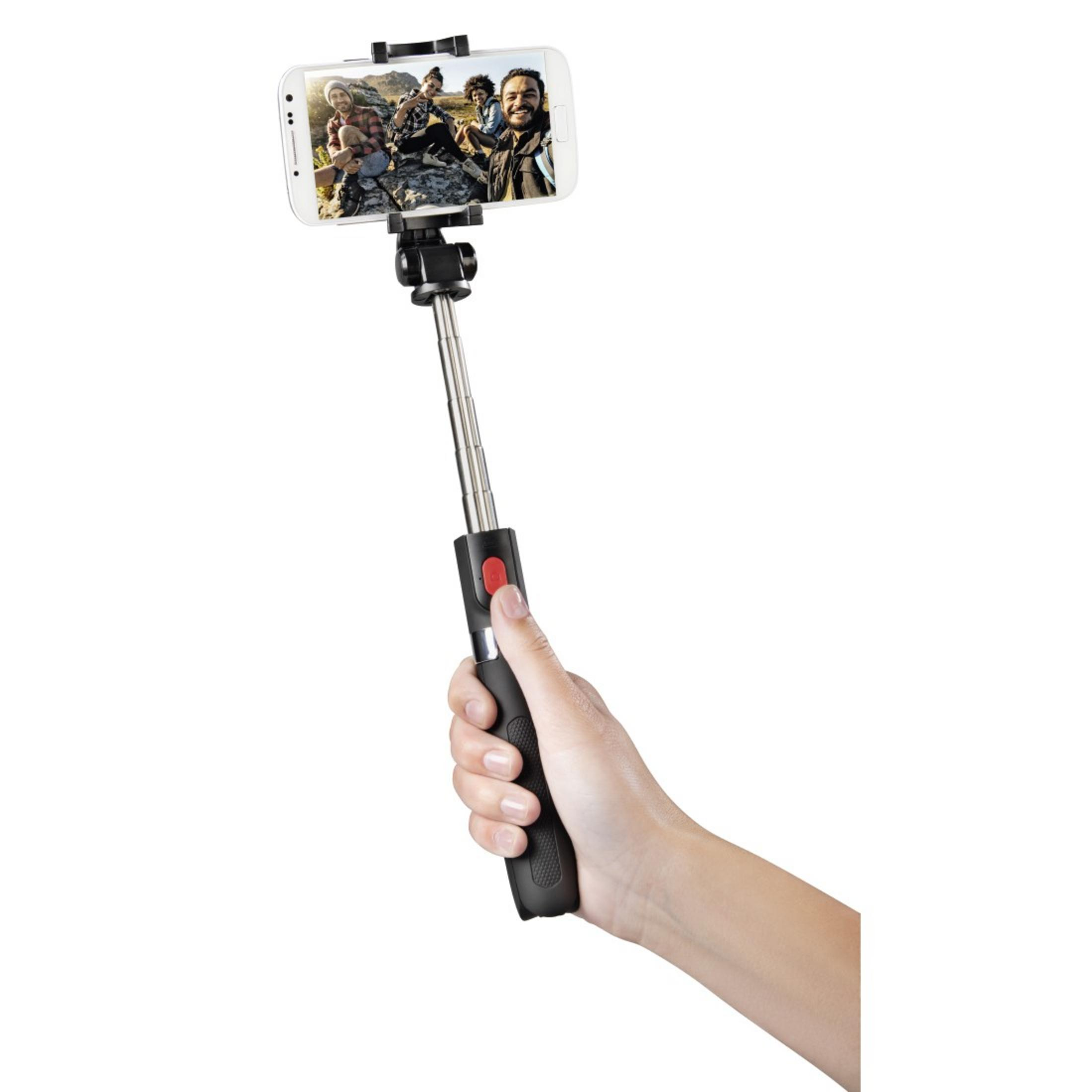Una persona tiene un bastone per selfie con uno smartphone che mostra una foto di gruppo su sfondo bianco.