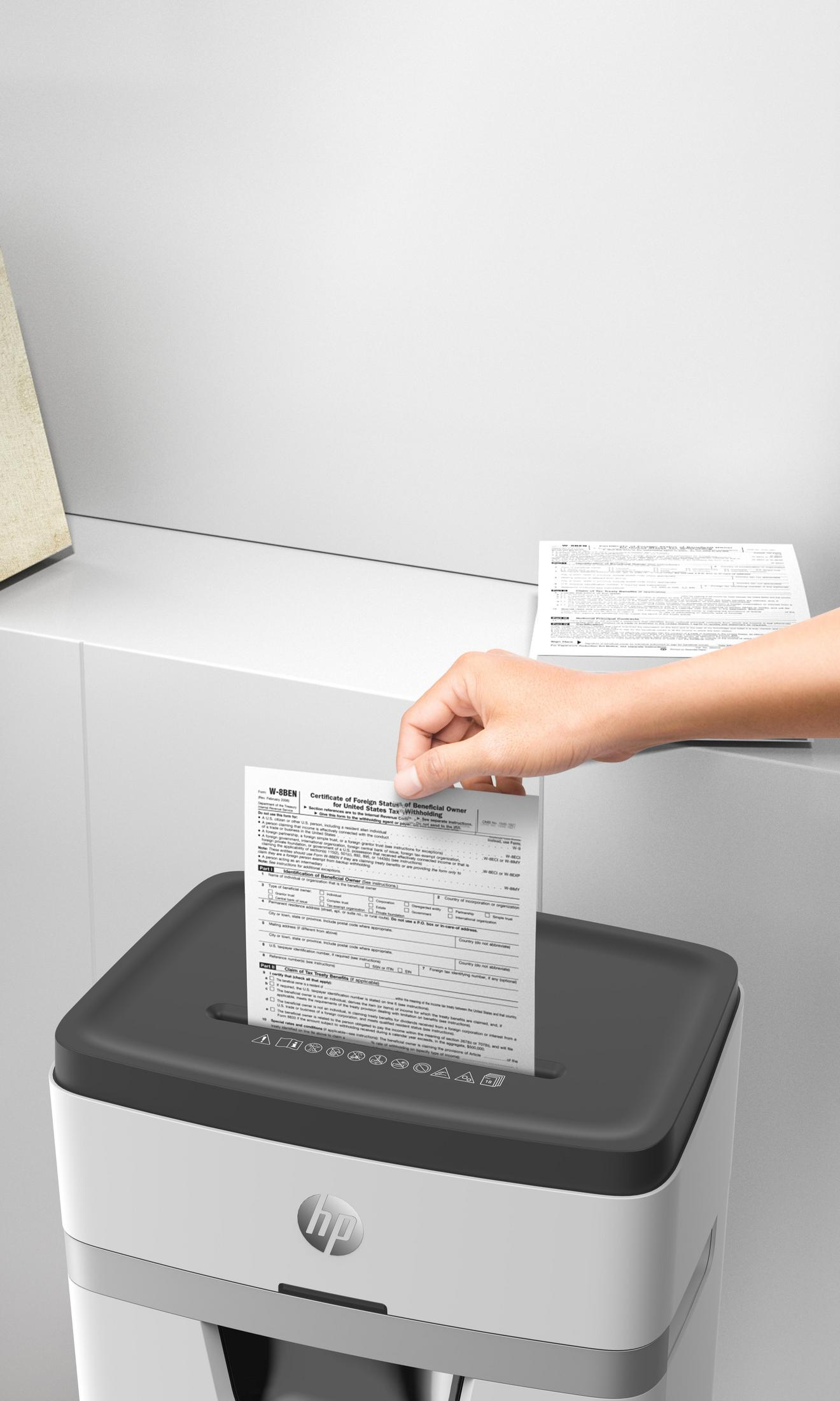 Eine Hand, die ein Papier in einen Aktenvernichter einführt. Im Hintergrund eine weiße Wand.