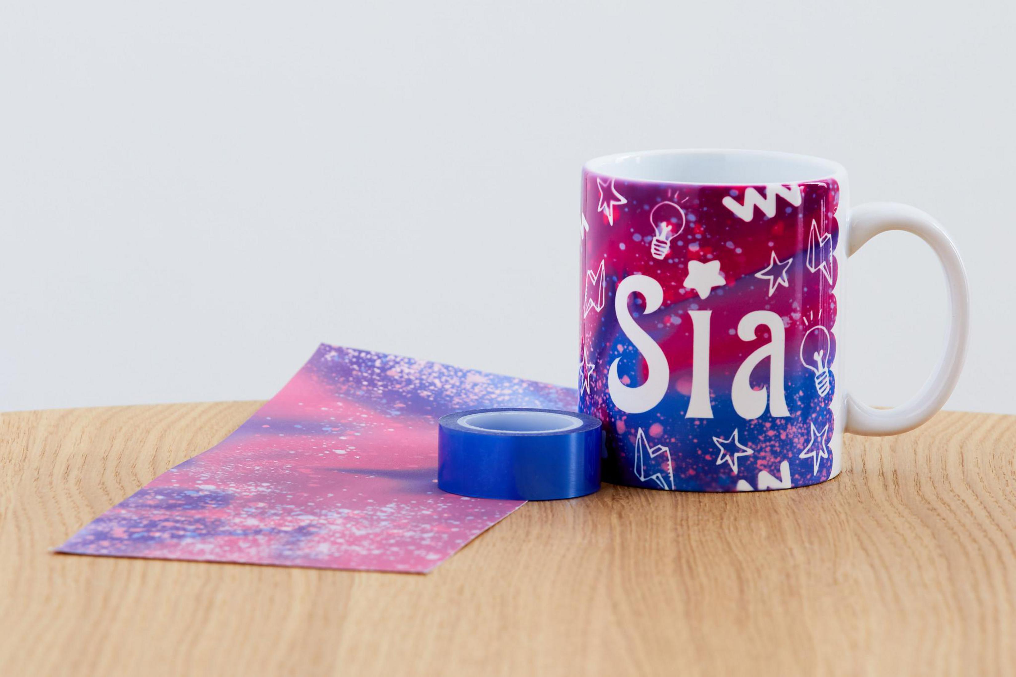 Una tazza con il nome "Sia", carta e nastro adesivo su un tavolo di legno.