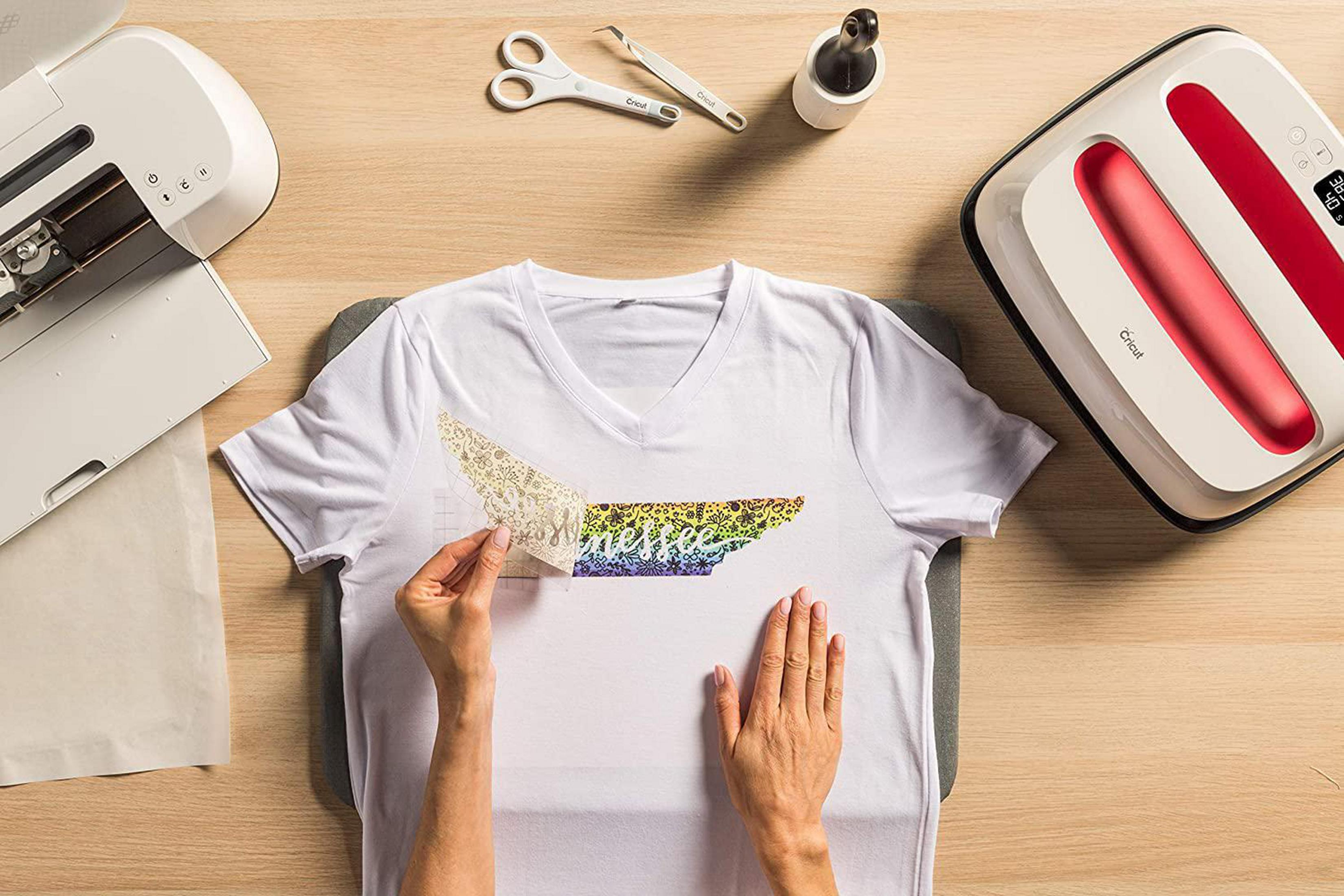 Hände, die ein Design mit einer Transferpresse auf ein weißes T-Shirt aufbringen. Cricut und Zubehör.