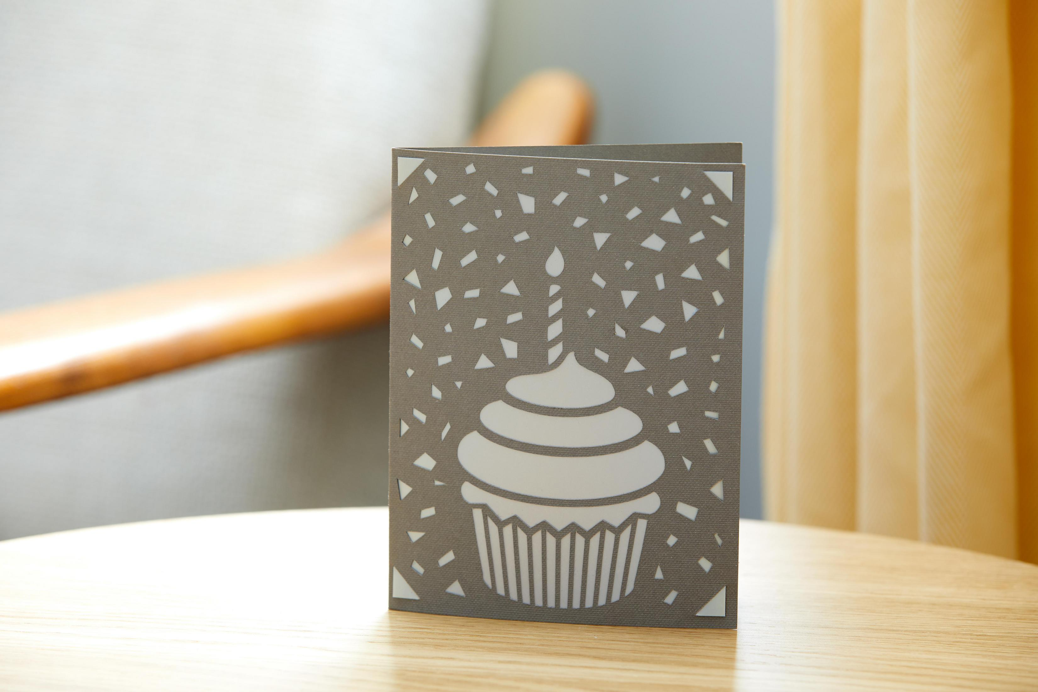 Graue Geburtstagskarte mit Cupcake-Design auf einem Holztisch.