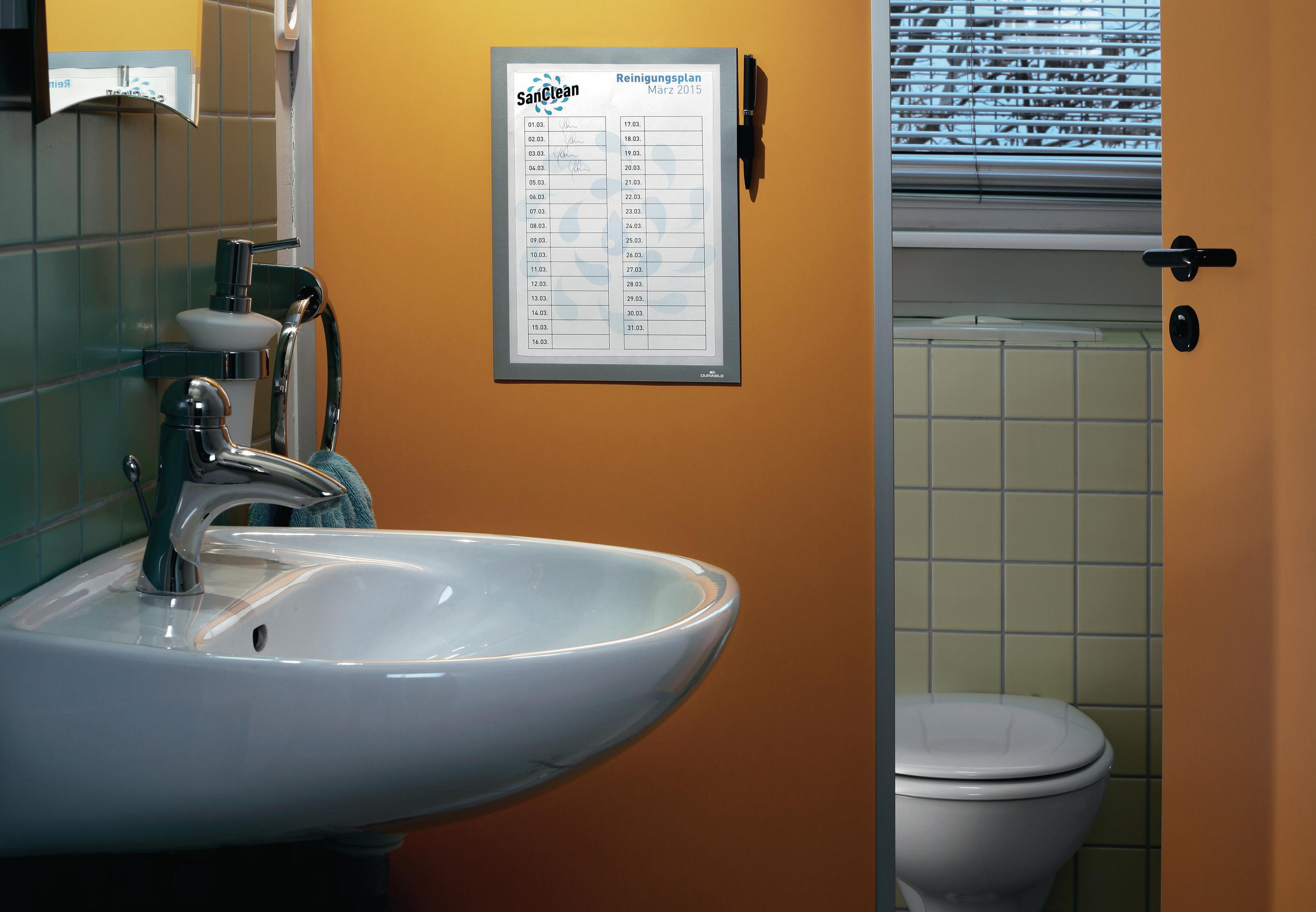 Ein Badezimmer mit einem Reinigungsplan an der Wand über dem Waschbecken und einer Toilette im Hintergrund.