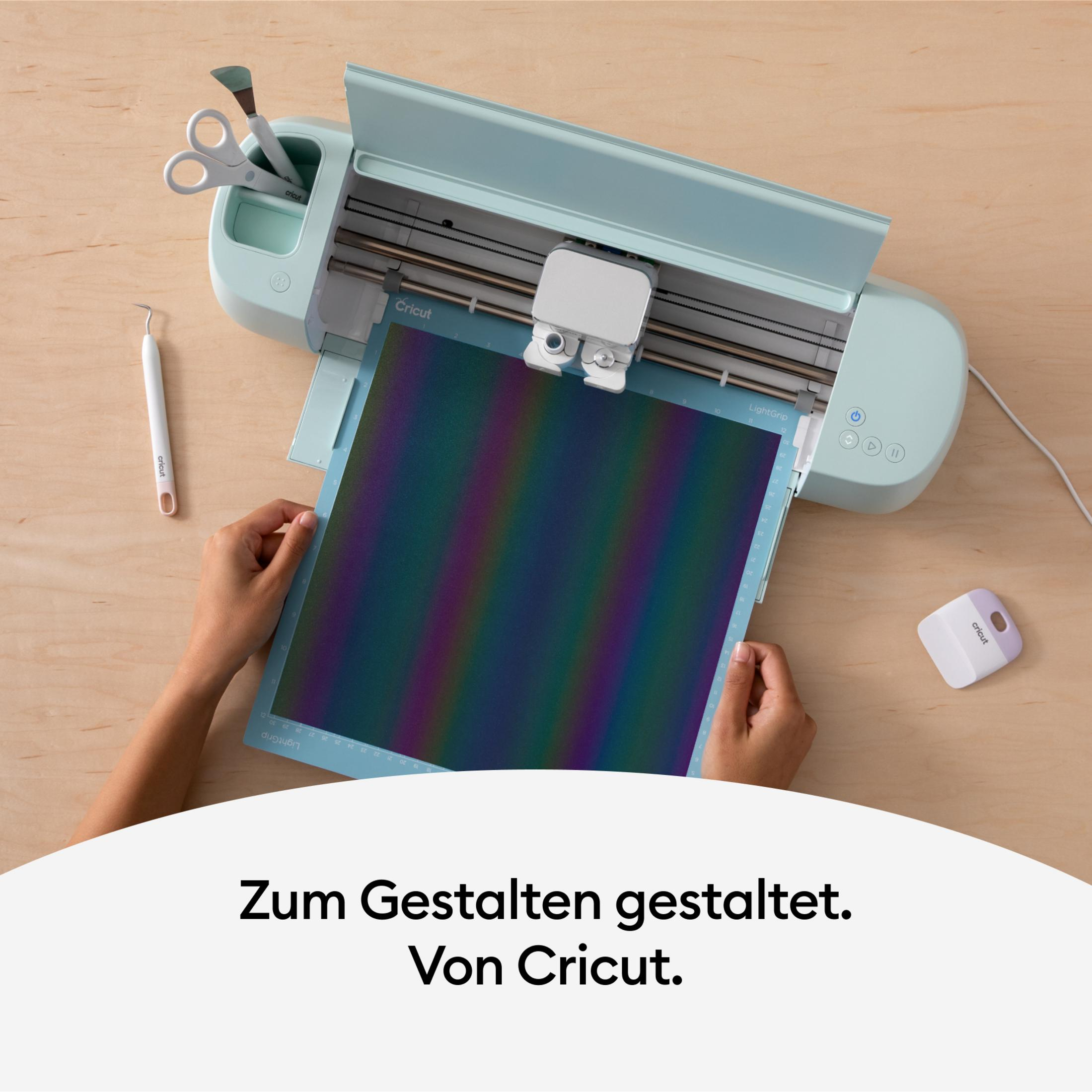 Draufsicht auf eine Cricut-Maschine mit farbenfrohem, gemustertem Material. Hände arbeiten an der Maschine.