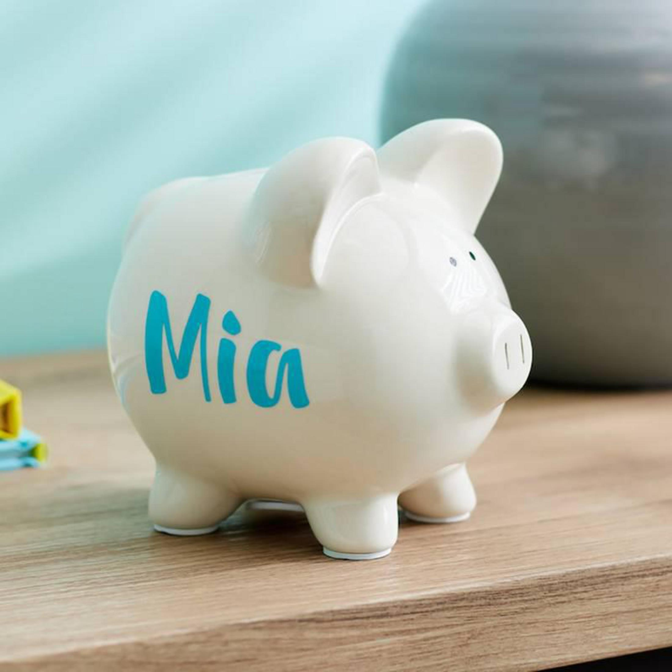 Ein weißes Sparschwein mit dem Namen 'Mia' in türkisfarbenen Buchstaben auf Holz.