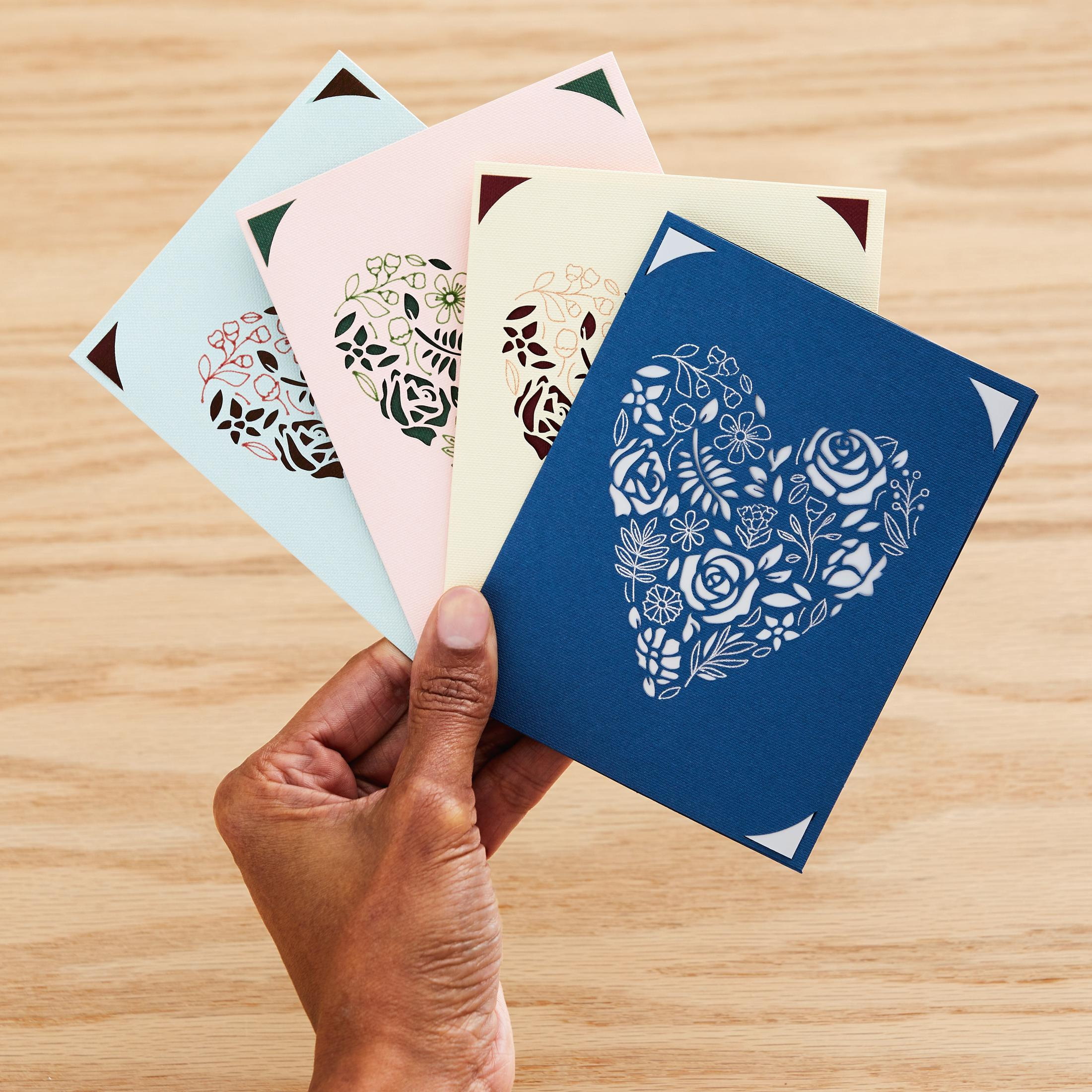 Hand, die vier farbige herzförmige Karten hält. Jede Karte hat ein Blumendesign.