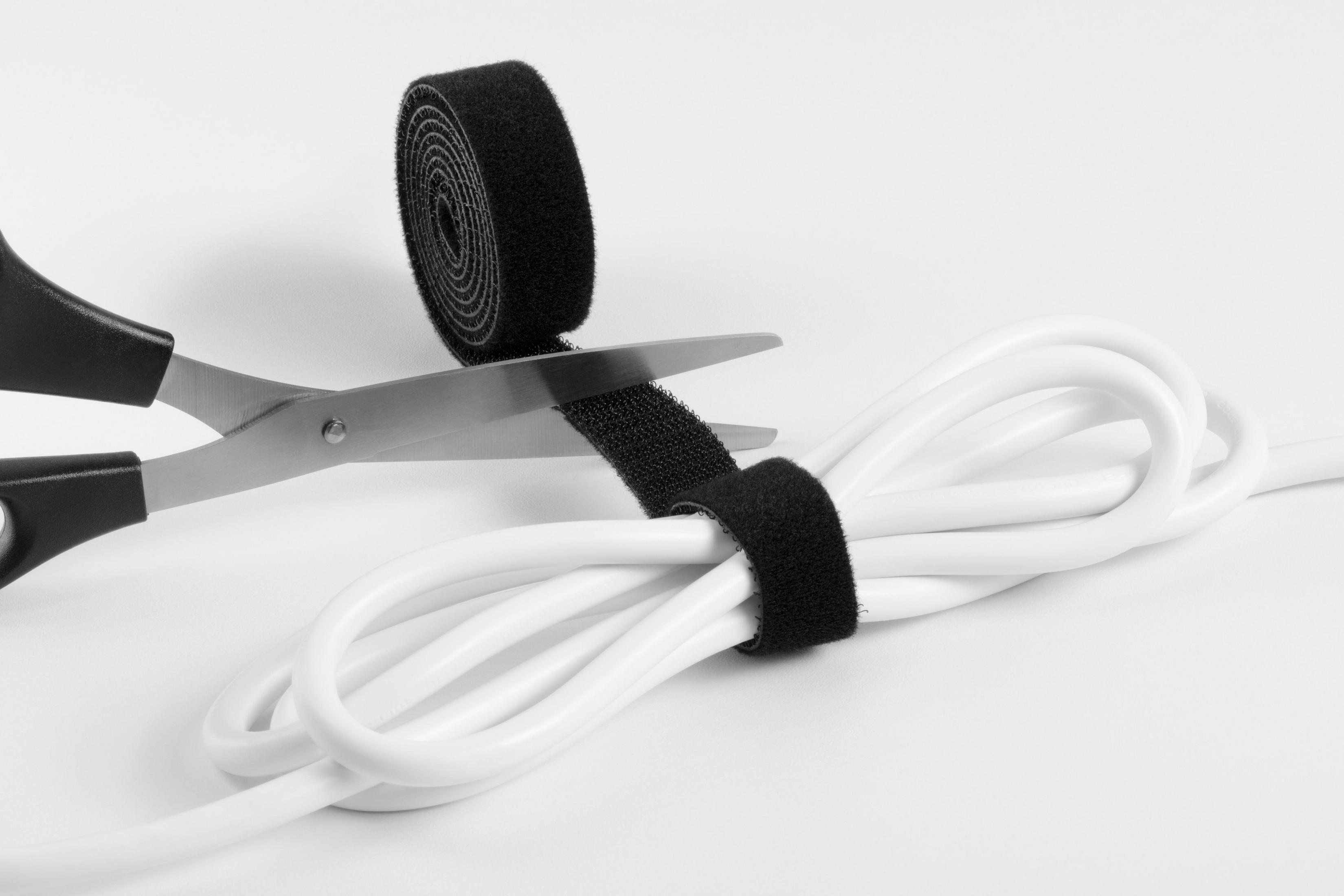 Schere schneidet schwarzen Klettverschluss um ein weißes Kabel. Weißer Hintergrund.