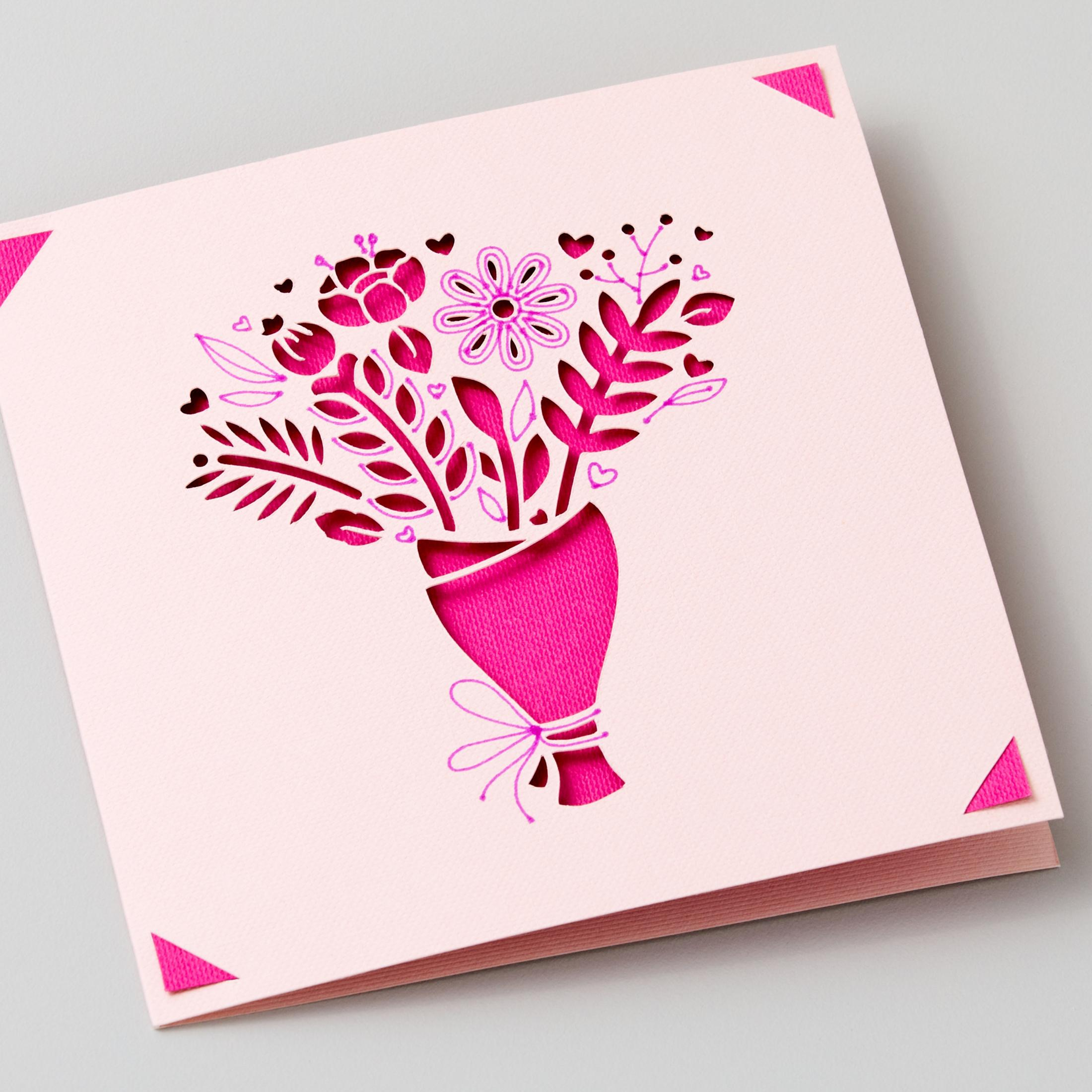 Rosa Grußkarte mit einem ausgeschnittenen Blumenstrauß-Design und rosa Akzenten in den Ecken.