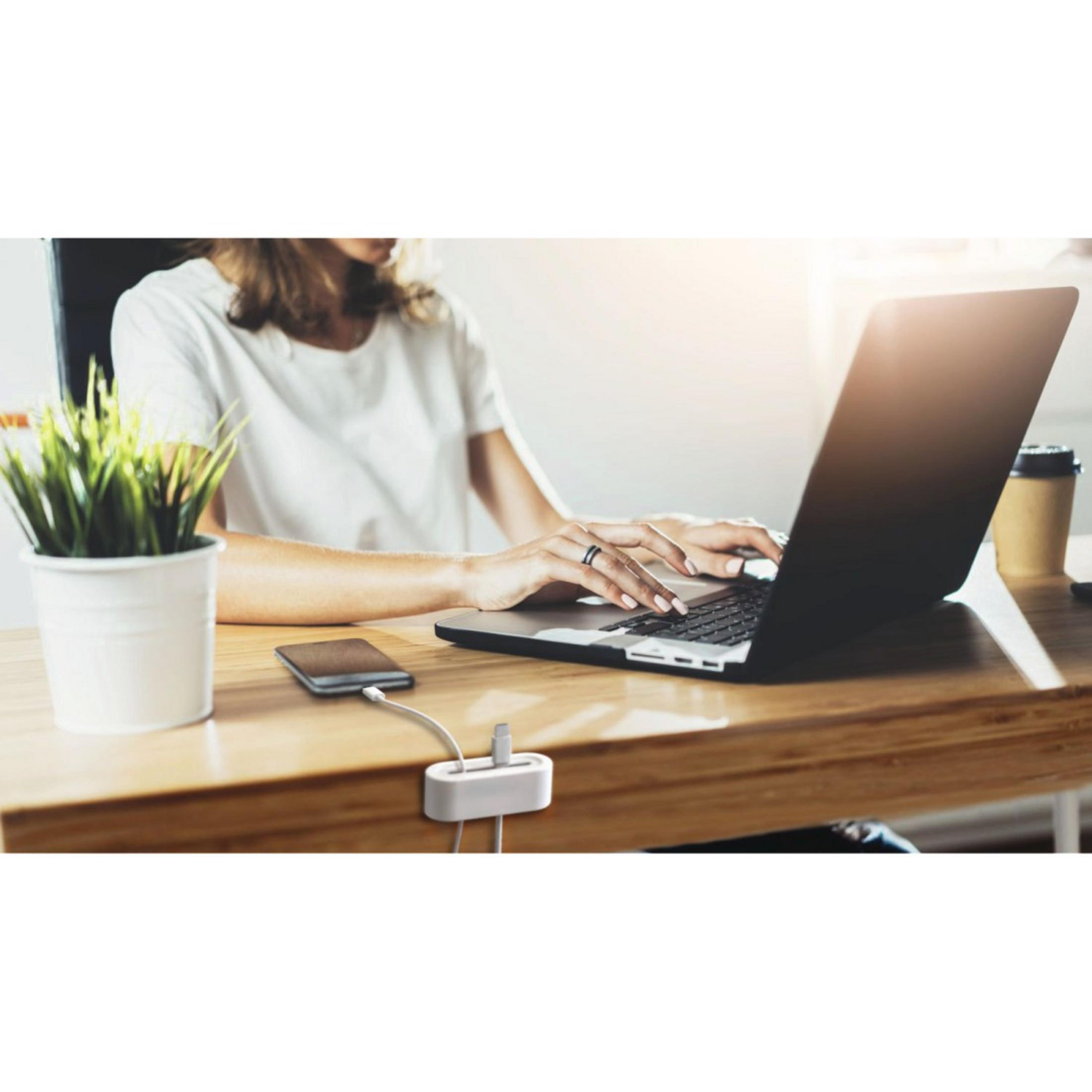 Osoba korzystająca z laptopa przy biurku, z hubem ładującym i telefonem obok.