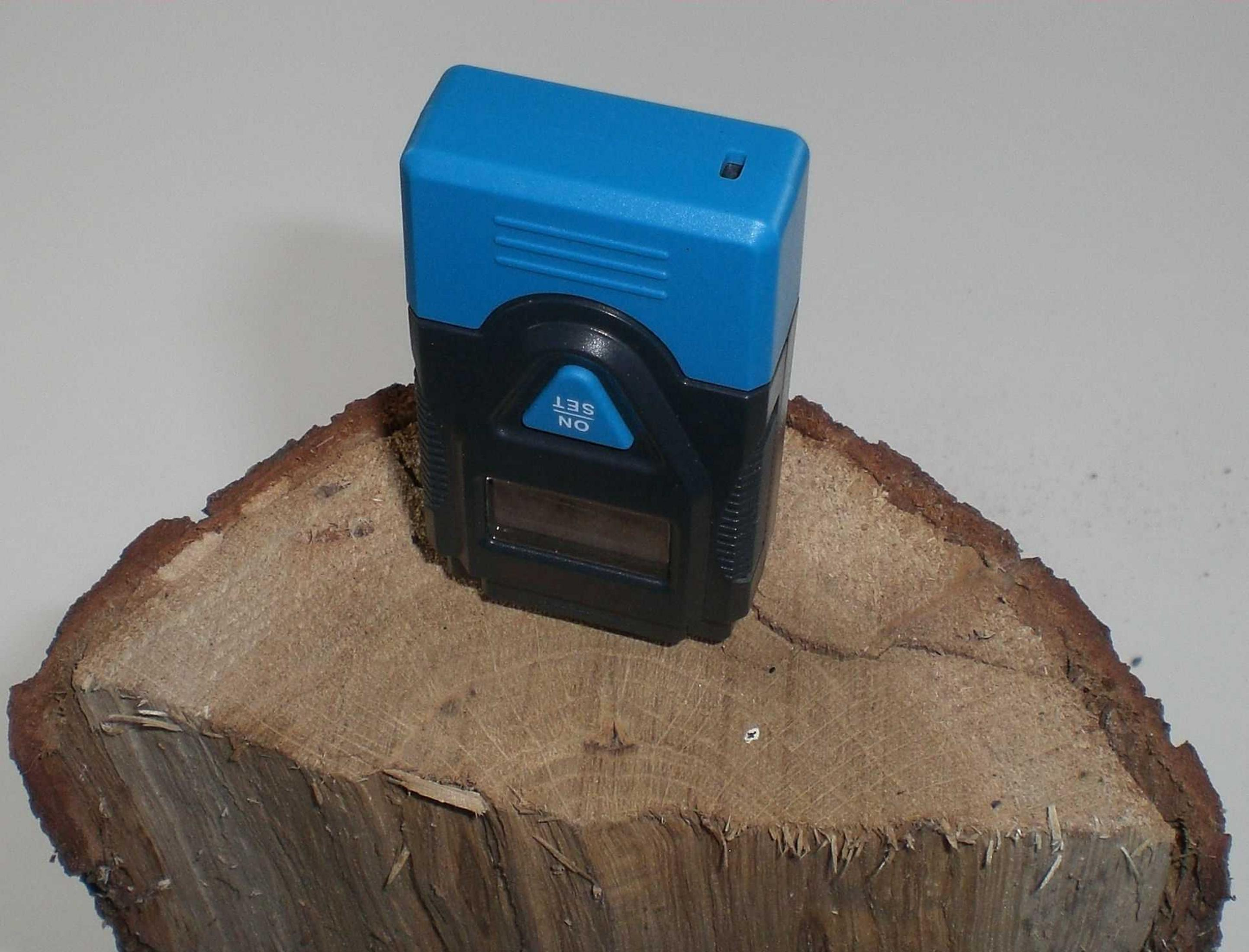 Ein blau-schwarzes Gerät auf einem Holzscheit. Es hat eine Digitalanzeige und Knöpfe mit 'ON' und 'SET'.