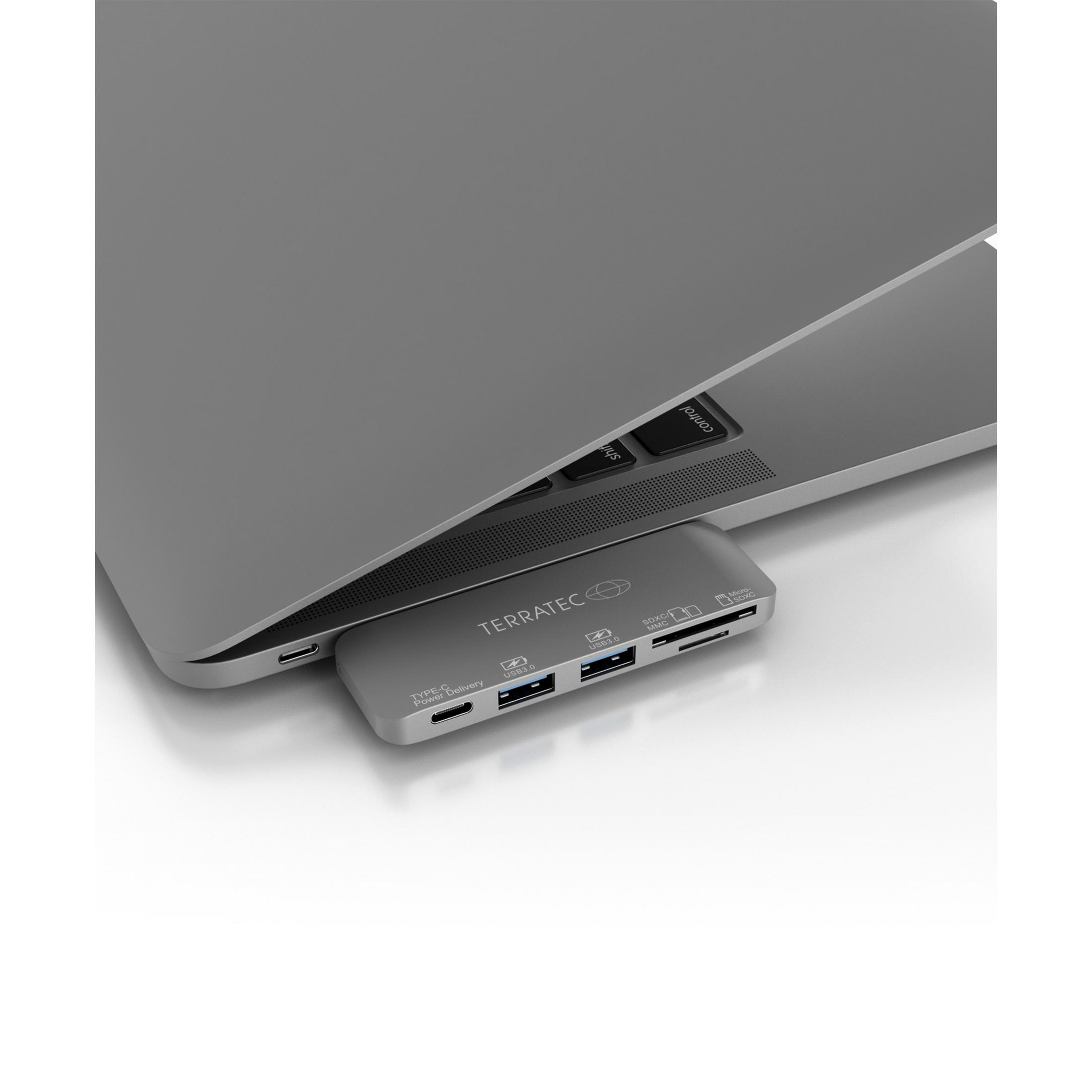 Ein grauer Laptop mit einem silbernen Hub, der USB-Anschlüsse und andere Verbindungen zeigt.